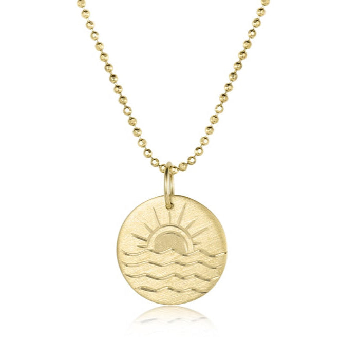 Gold necklace with a circular pendant featuring a sun and wave design on a white background by Julez Bryant