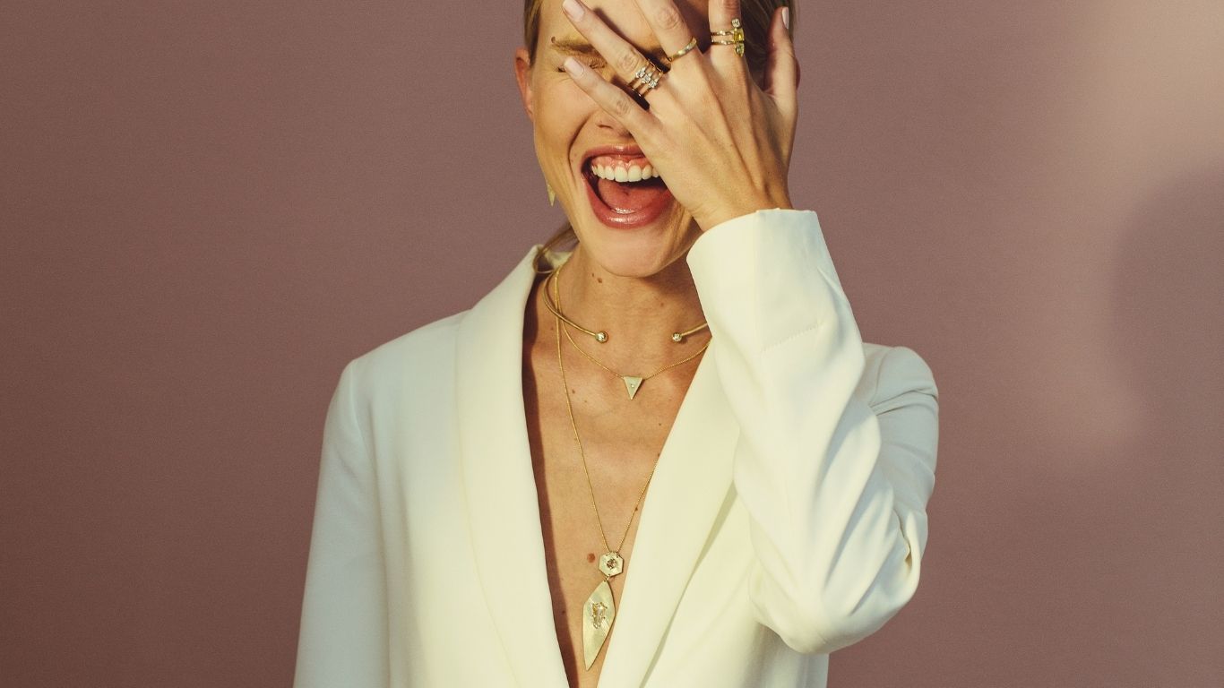 Woman in a white blazer with gold jewelry on a plain background
