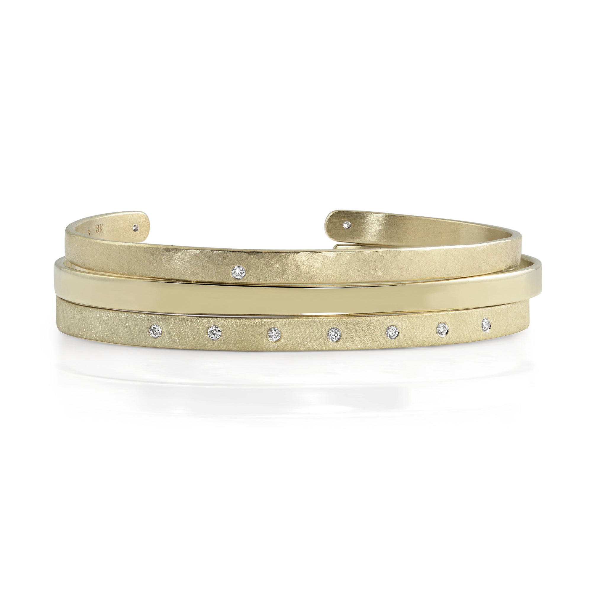14k yellow gold open cuff bracelet with white diamonds stacked with a hammered open cuff bracelet with white diamond accents and a shiny open cuff bracelet on white background