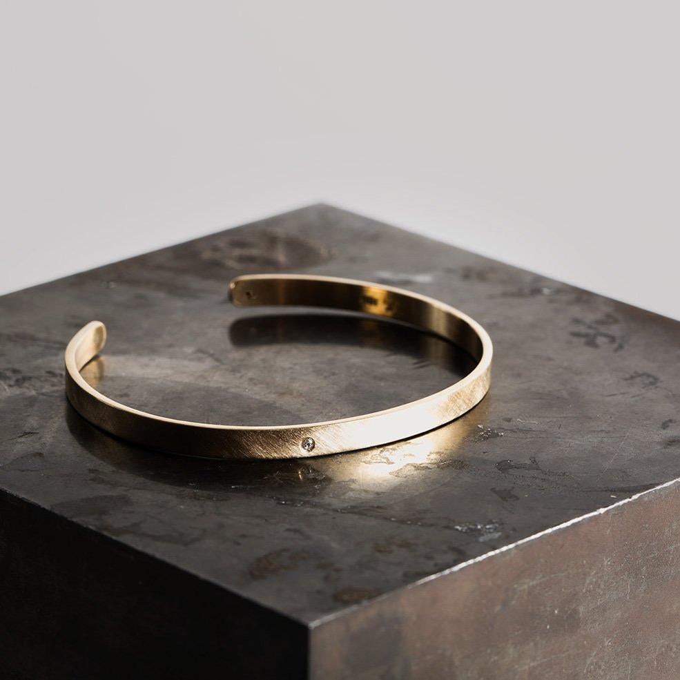 14k yellow gold hammered open cuff bracelet with single white diamond accent on dark stone background