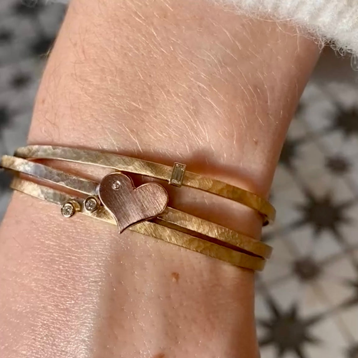 14k yellow gold hammered open cuff bracelet with two bezel set white diamonds stacked with two hammered open cuff bracelets with a rose gold heart with a white diamond accent and a baguette white diamond accent on model in lifestyle shot