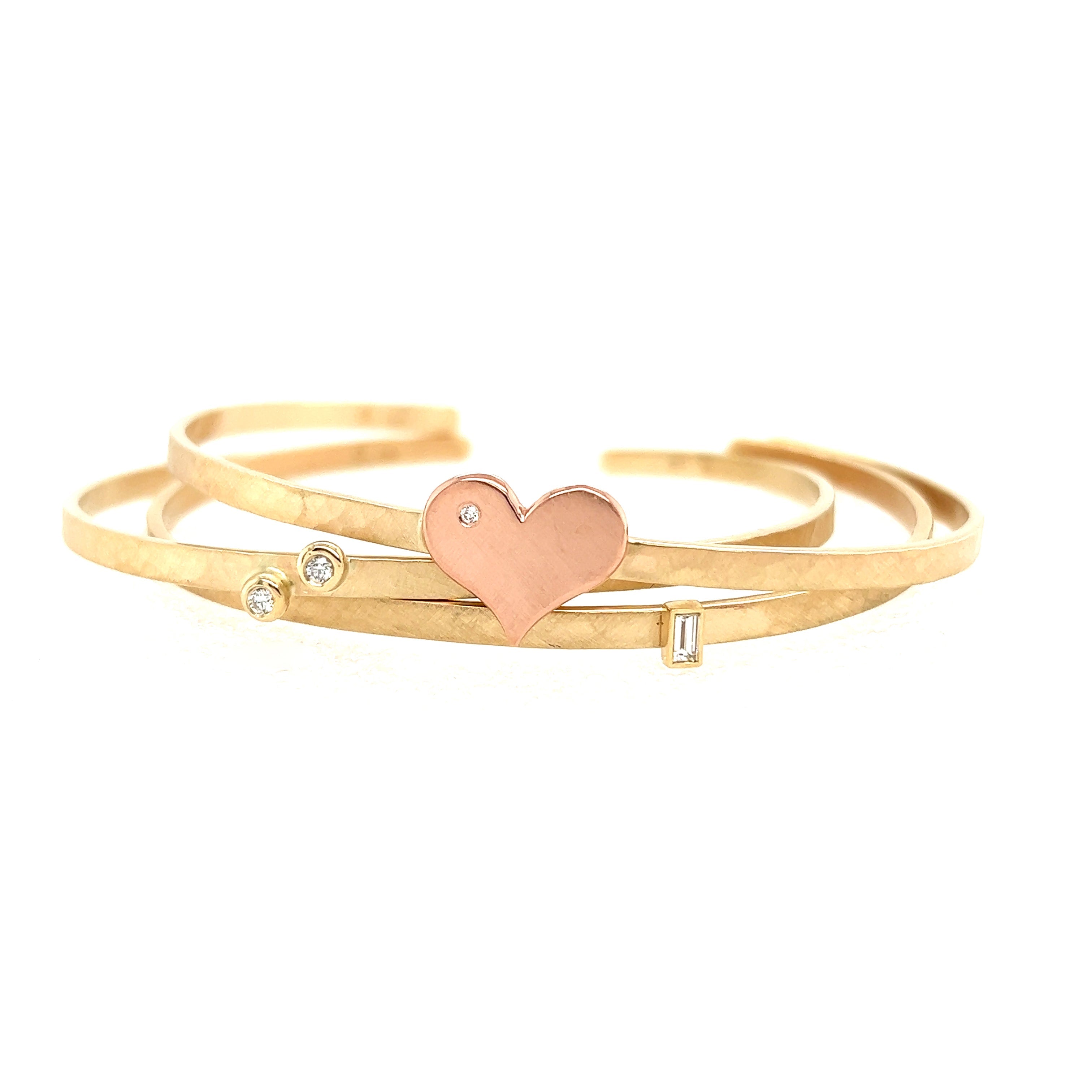 14k yellow gold hammered open cuff bracelet with two bezel set white diamonds stacked with a hammered open cuff bracelet with a rose gold heart with a white diamond accent and a hammered open cuff bracelet with a baguette white diamond on white background