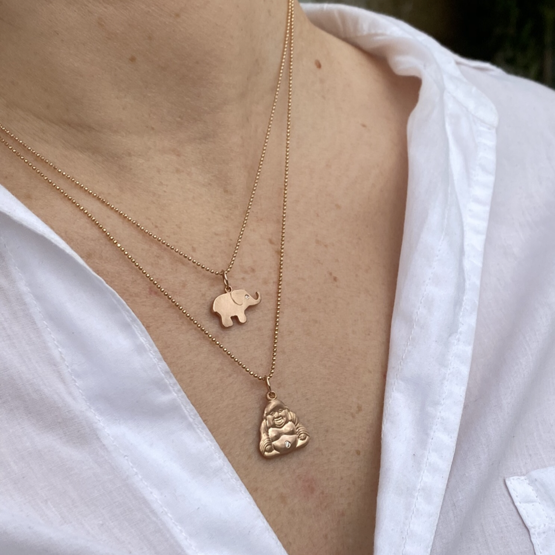 14k rose gold small buddha charm pendant with white diamond accent on diamond cut ball chain paired with 14k rose gold ello baby charm pendant on lifestyle shot