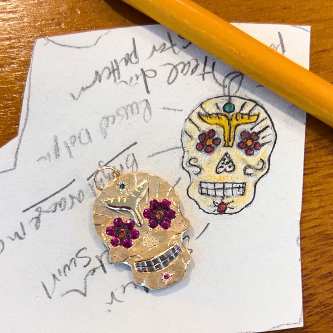 14k yellow gold ghostrider pendant with pink and orange and teal gemstones and hand etching next to a sketch of the ghostrider