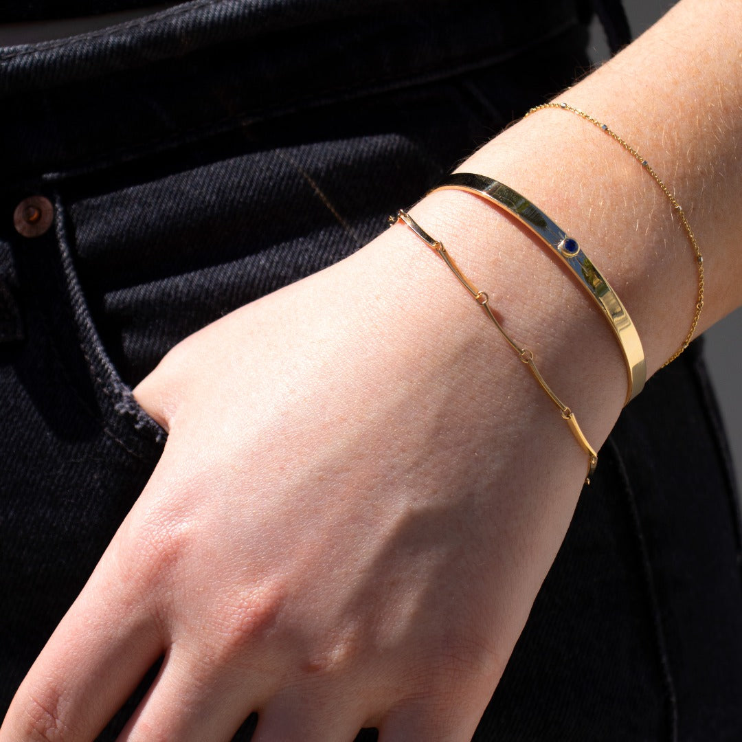 14k yellow gold flat bar link bracelet stacked with shiny yellow gold cuff bracelet with hand etched sunburst and bezel set gemstone and icecube chain bracelet on model in lifestyle shot