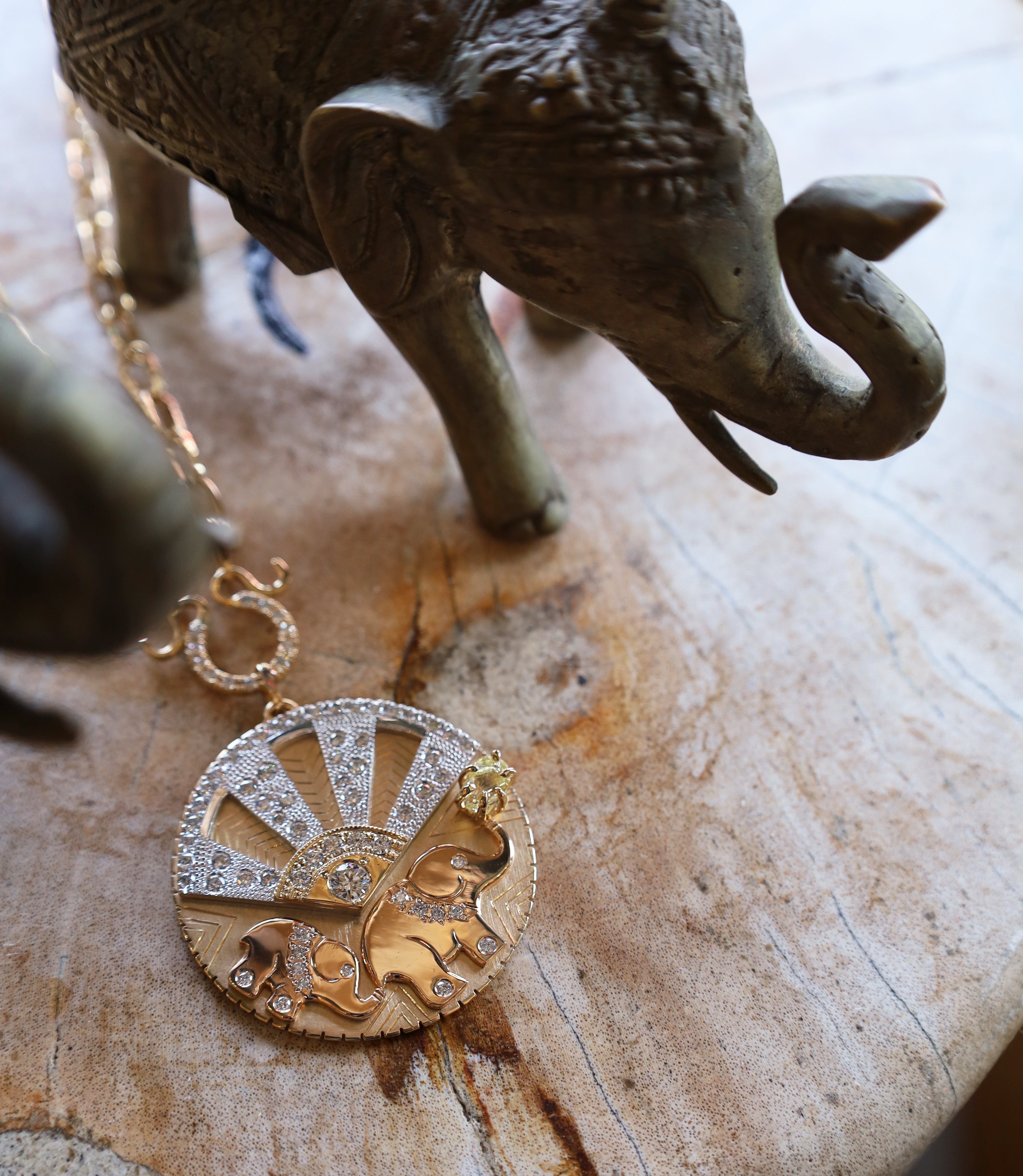 Gold necklace with a decorative pendant on a wooden surface with an elephant figurine.