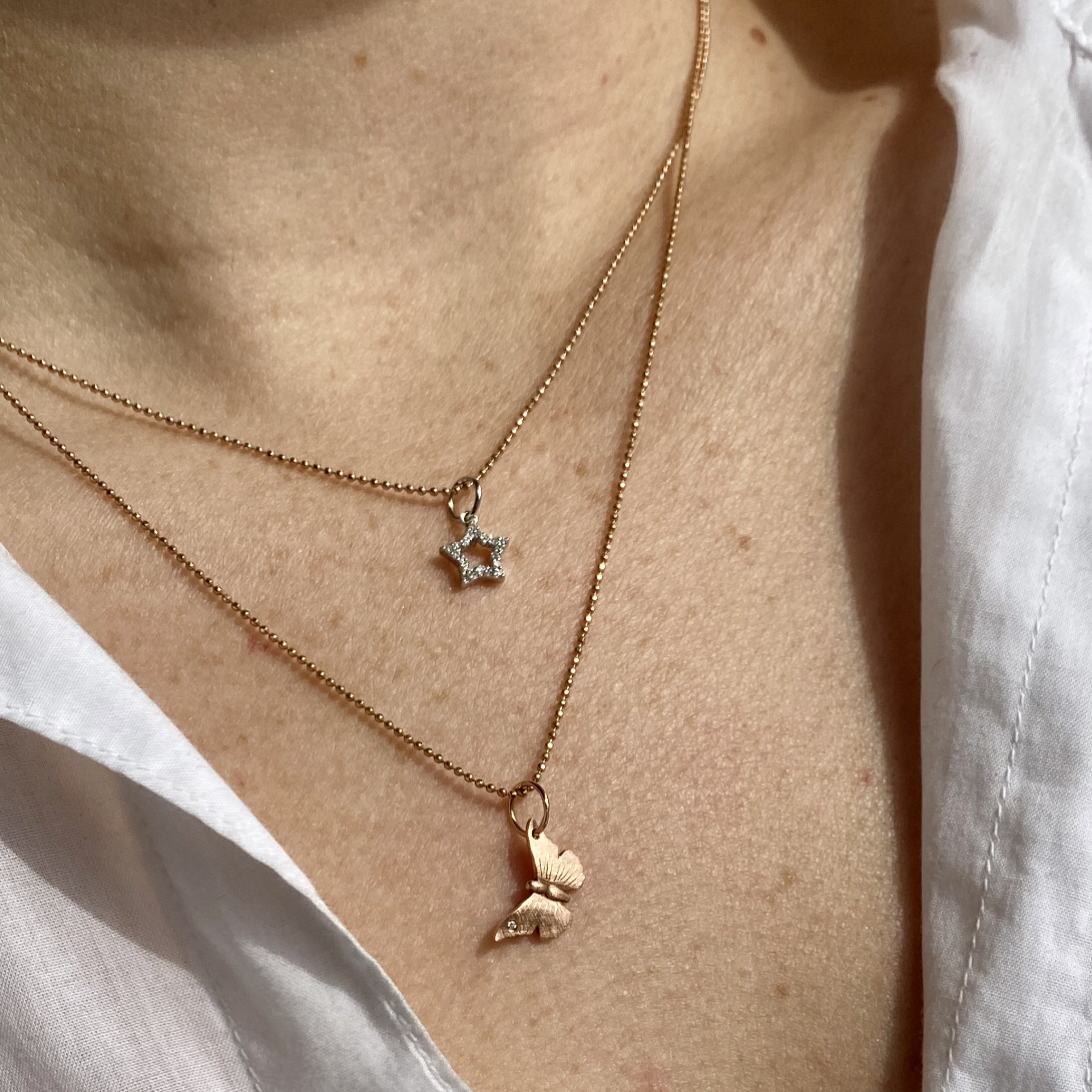 14k gold star charm pendant with white diamonds on a ball chain paired with the anna baby butterfly pendant on model in lifestyle shot