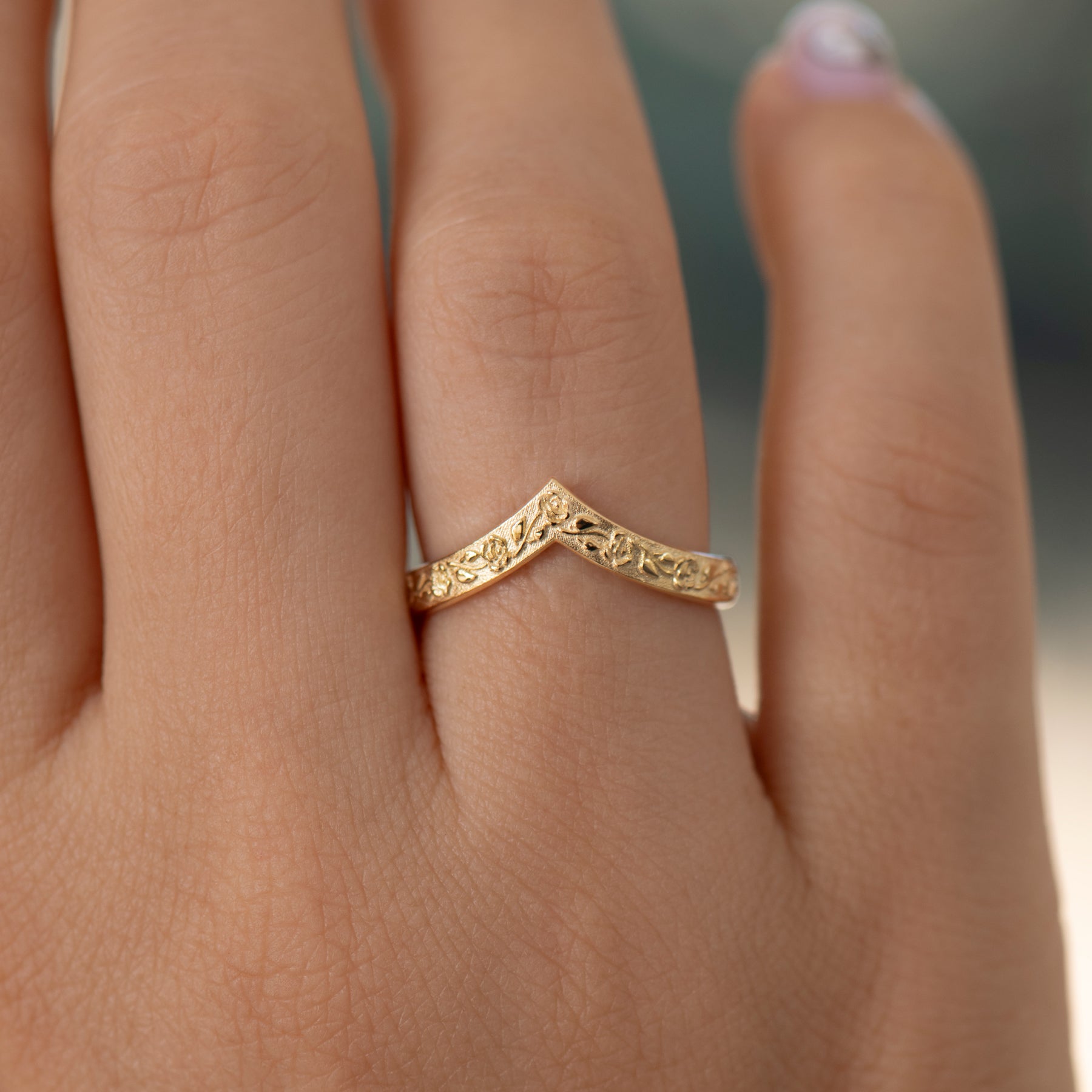 Gold ring with intricate design on a person's finger against a blurred background
