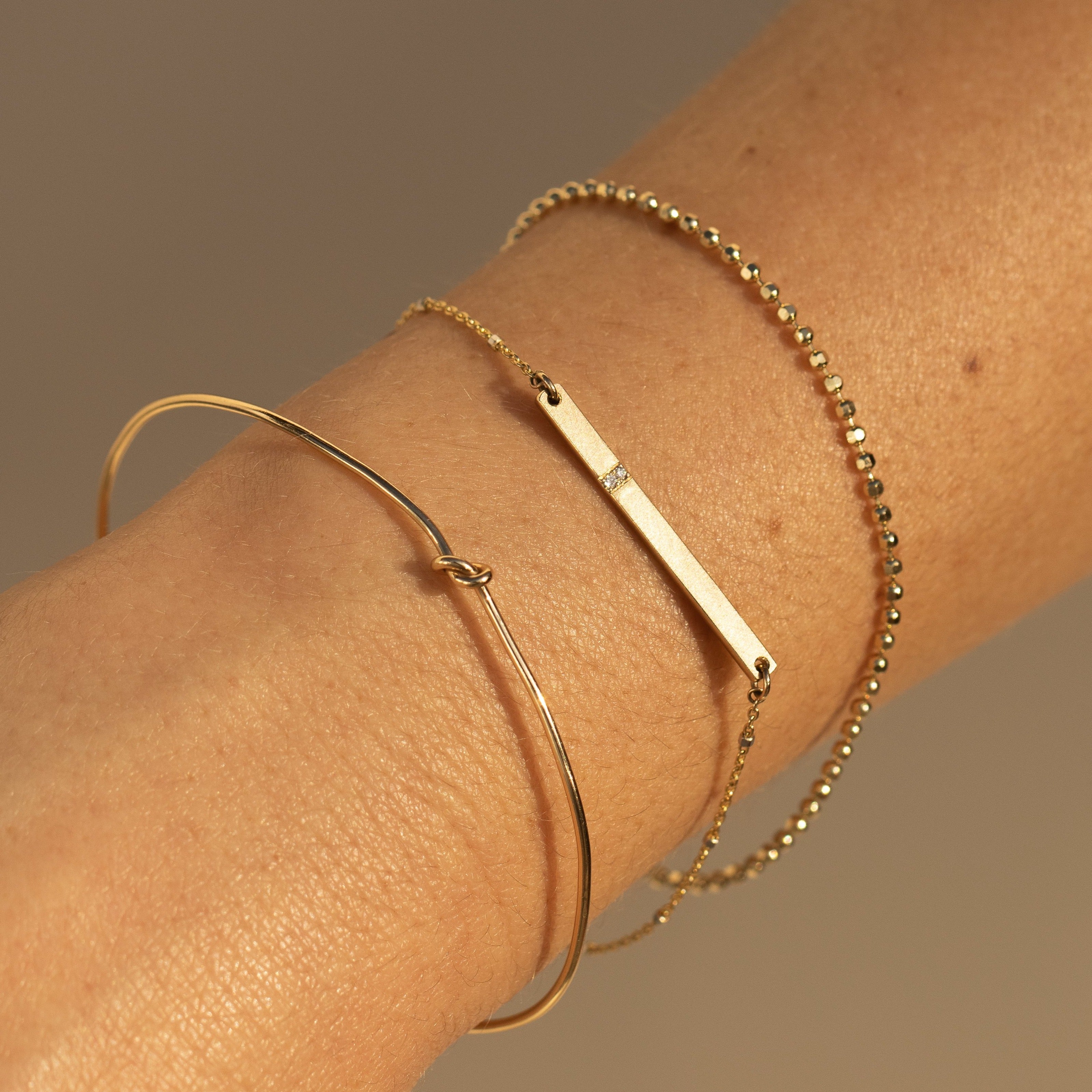 14k yellow gold bar bracelet with white diamond accents on ice cube chain stacked with diamond cut ball chain bracelet and gold knot wire bracelet on model in lifestyle shot
