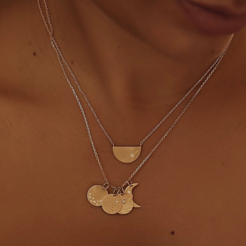 14k gold necklace stack featuring round pendant with hand etched tree design and white diamond sunburst on rolo chain on a model in lifestyle shot