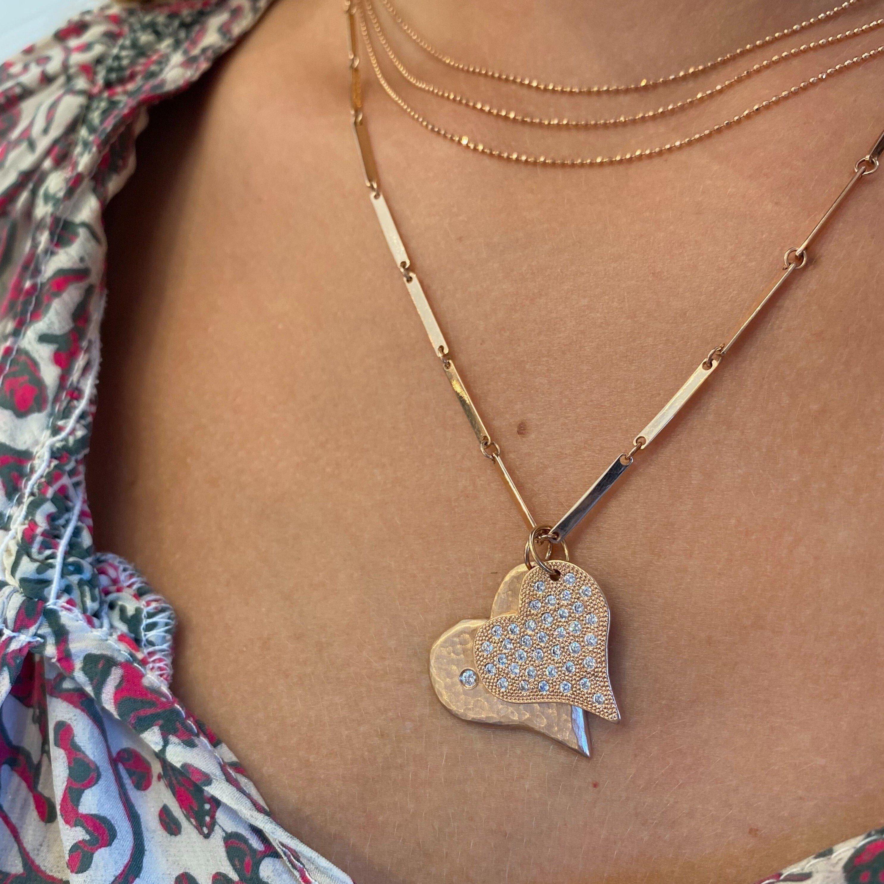 14k gold chai necklace stacked with two heart pendants with beaded and hammered textures and scattered white diamonds on a doey chain on a model in a lifestyle shot
