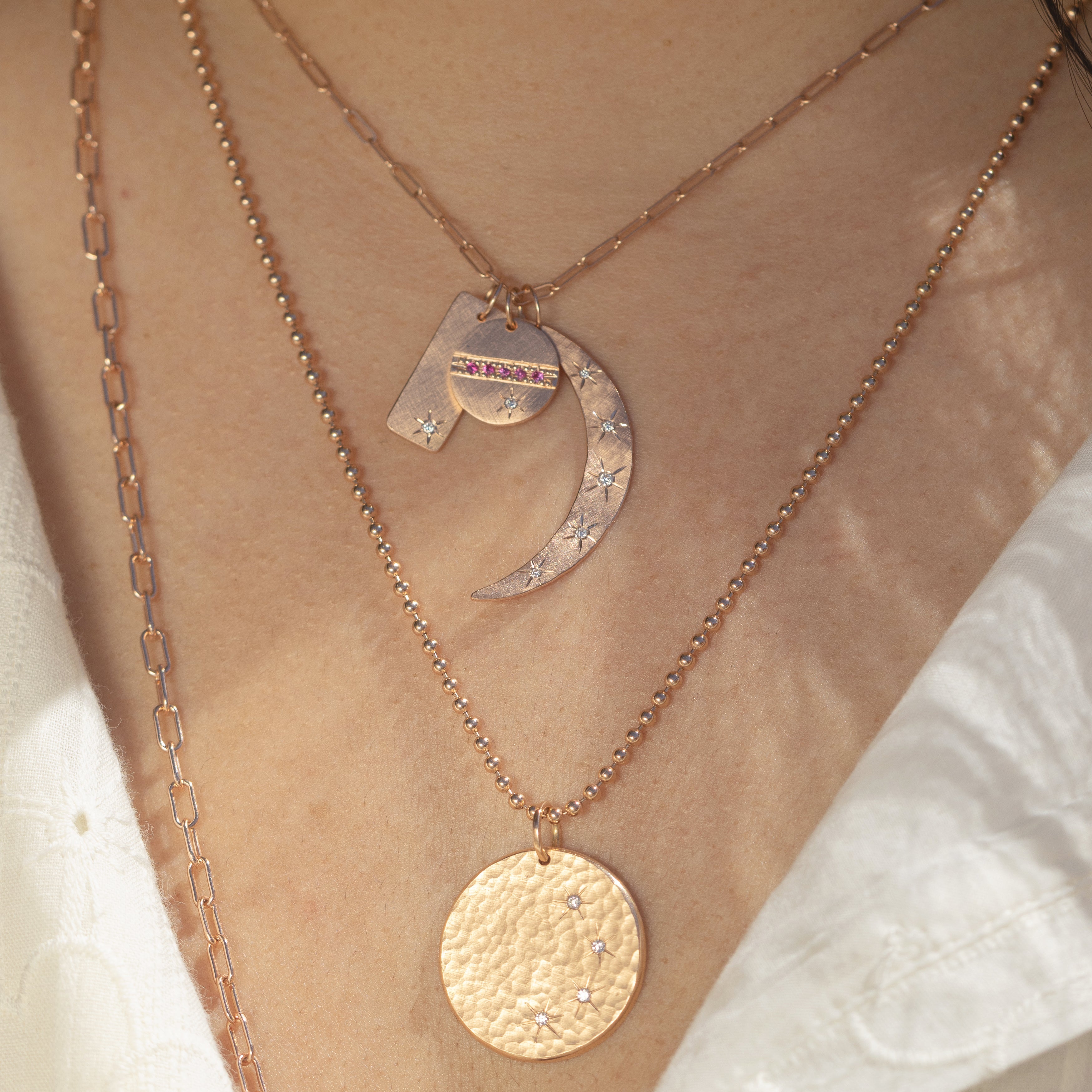 14k yellow gold hammered crescent moon pendant with scattered white diamonds and hand etched starbursts paired with niki pendant and halo pendant on link chain stacked with round hammered pendant with white diamonds and hand etched starbursts on model in lifestyle shot