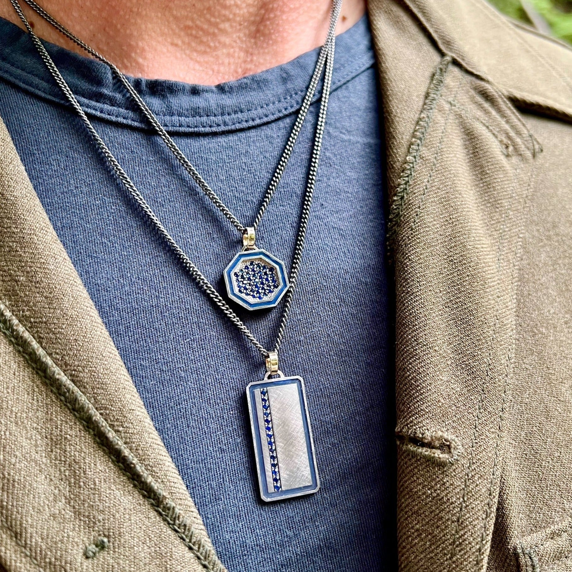 blackened sterling silver octagon pendant with colored gemstones and colored enamel border on 14k yellow gold jump ring stacked with a blackened sterling silver rectangle pendant with colored enamel border and blue gemstones with 14k yellow gold jump ring on model in lifestyle shot