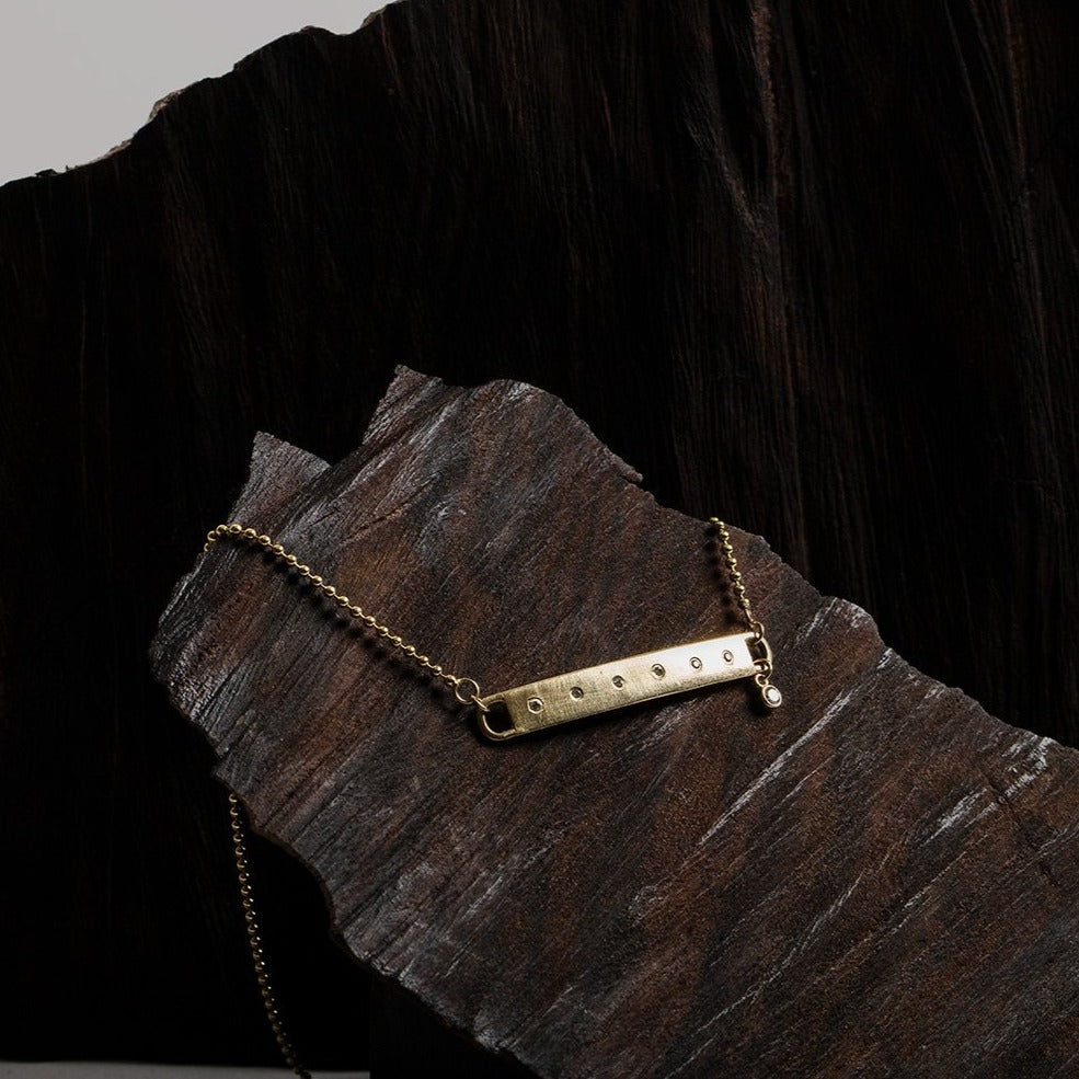 14k yellow gold bar wrap bracelet with white diamonds and wrap around ball chain with bezi accent charm on dark stone background