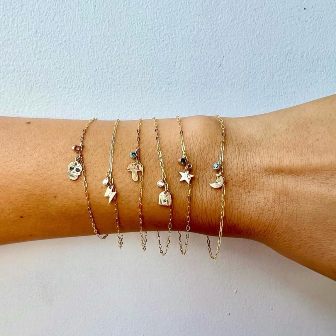 14k yellow gold teeny tiny teal diamond hummingbird charm bracelet with bezel set white diamond charm beside other teeny tiny bracelets on model in lifestyle shot