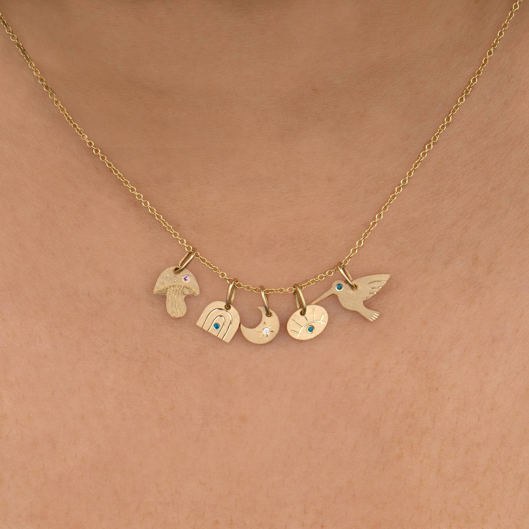 14k yellow gold hummingbird teeny tiny charm pendant with teal diamond on rolo chain paired with other teeny tiny charms on model in lifestyle shot