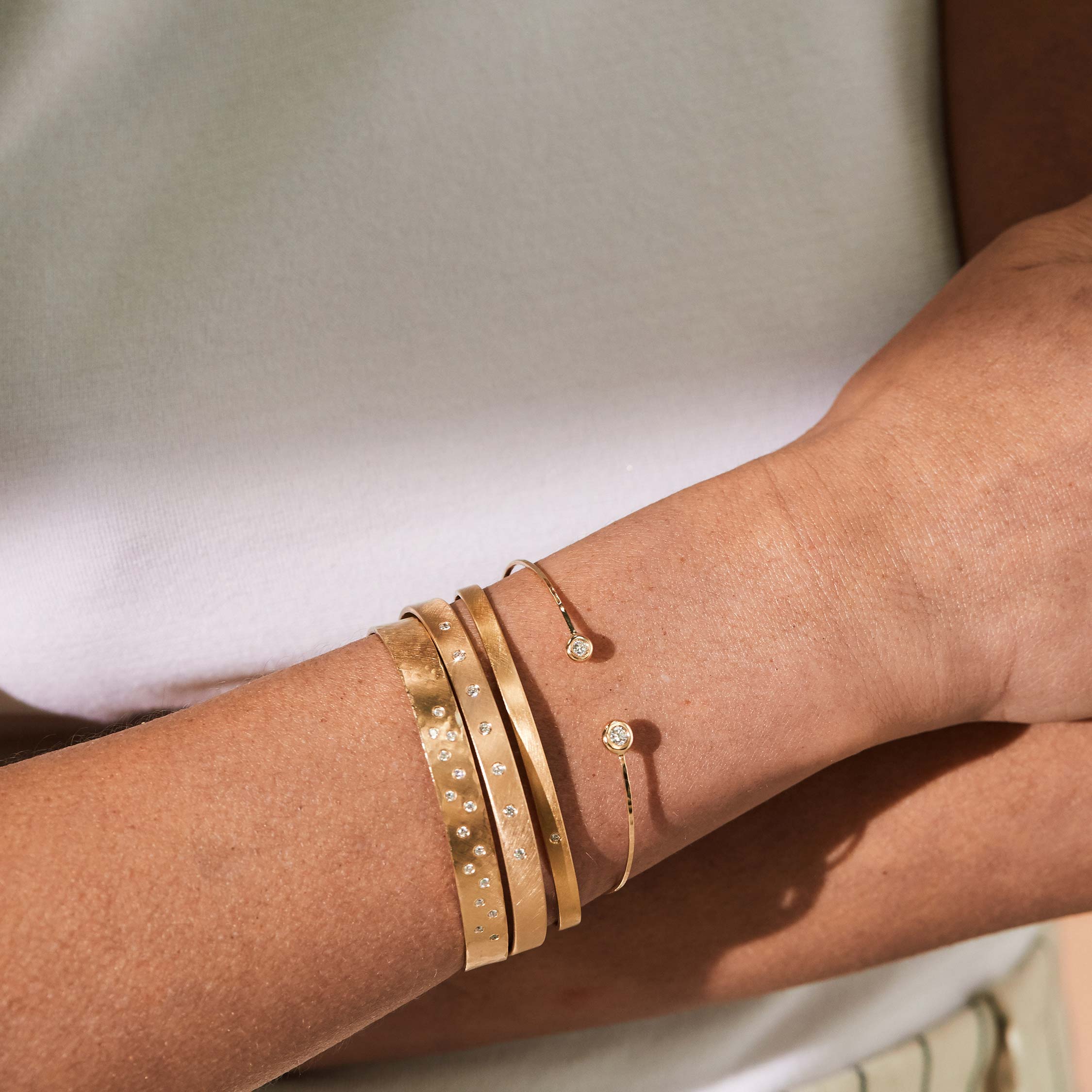 14k yellow gold wire paddle bracelet with two bezel set white diamonds stacked with three gold cuffs by julez bryant on model in lifestyle shot