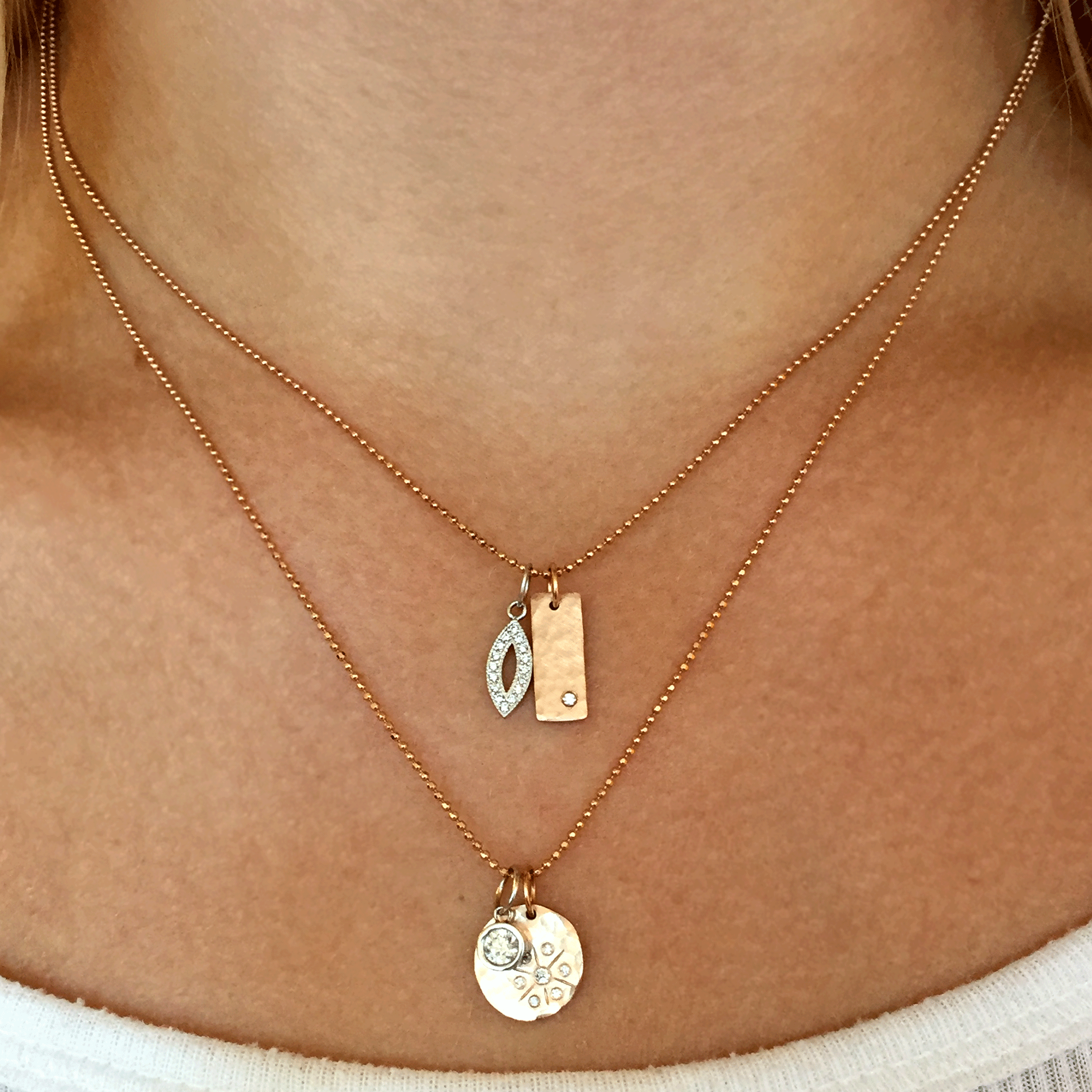 14k yellow gold round hammered pendant with white diamond starburst paired with white diamond bezi charm and stacked with marquis pendant and niki bar charm on model in lifestyle shot