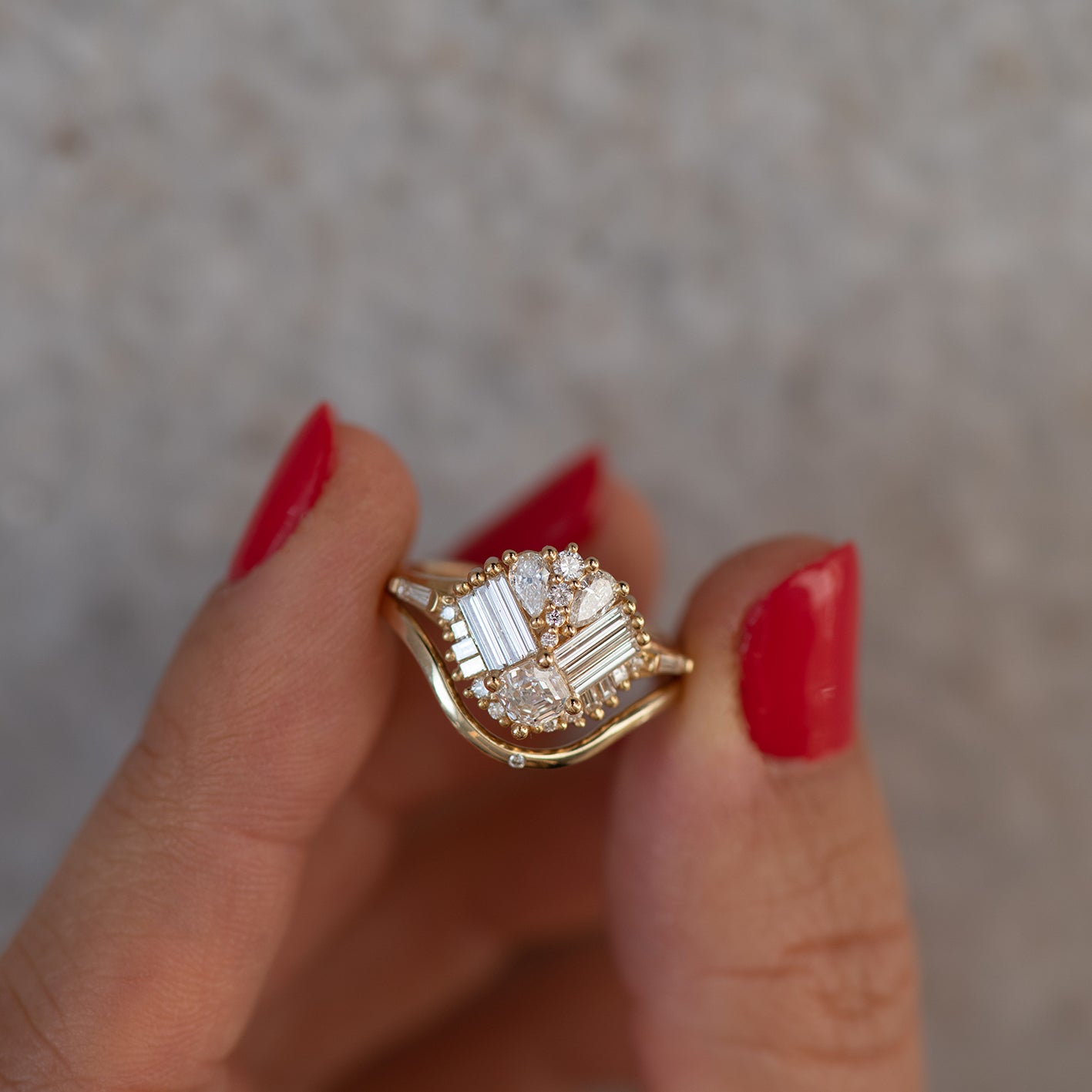 Front view 18k gold elaborate cluster ring with mixed shaped white diamonds including baguette, pear, princess, trapeze art deco feel, with simple shadow band closeup hel between models fingers