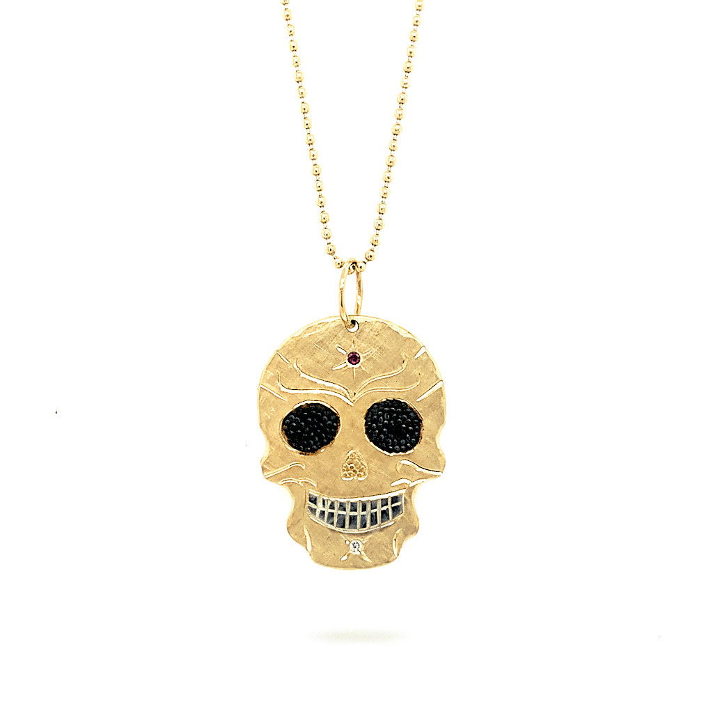 14k bright yellow gold small skull shaped pendant with pink and white gemstone accents with hand engraving and blackened beaded texture in the eyes hanging from diamond cut ball chain shown on white background