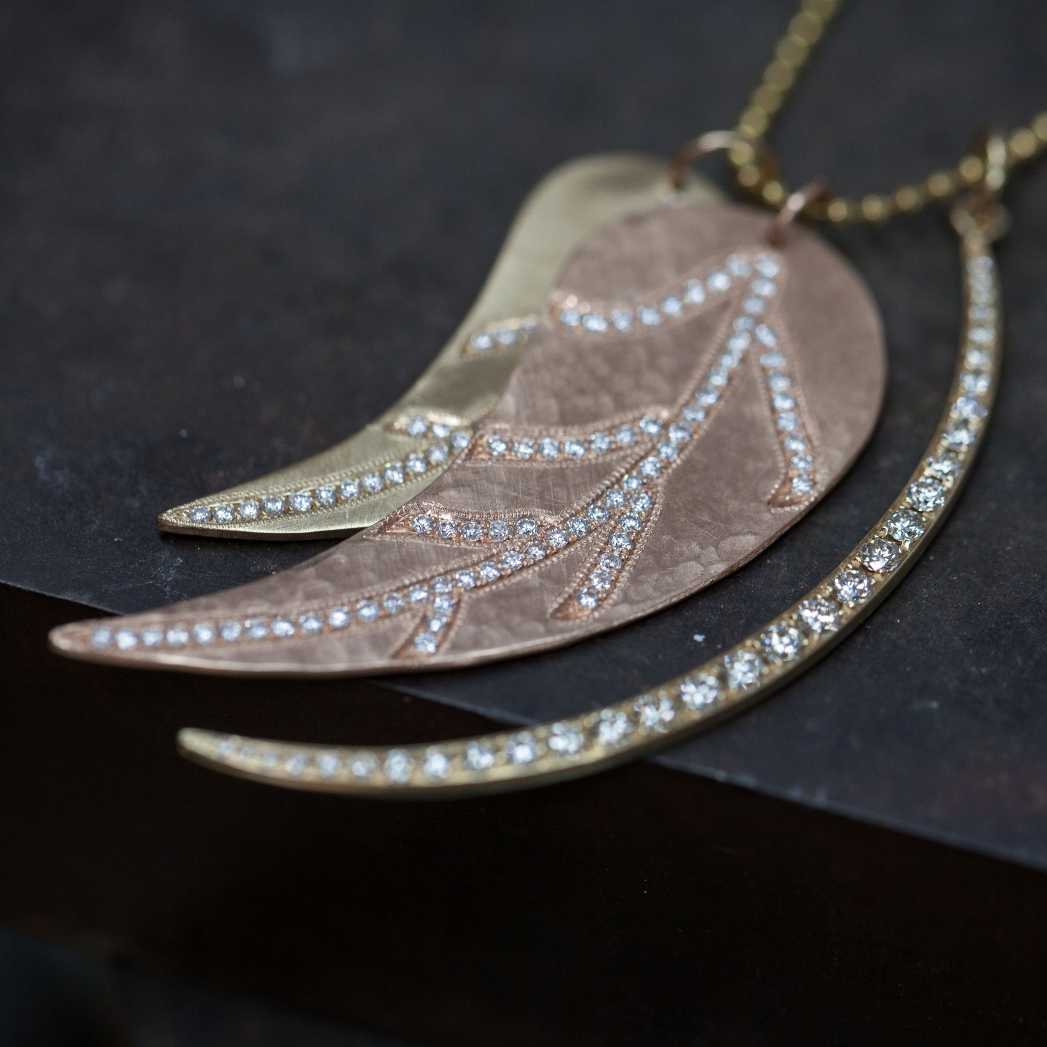 14k yellow gold crescent moon with white diamonds paired with rose gold hammered leaf pendant with white diamonds and yellow gold smaller leaf pendant with satin finish and white diamonds on dark background
