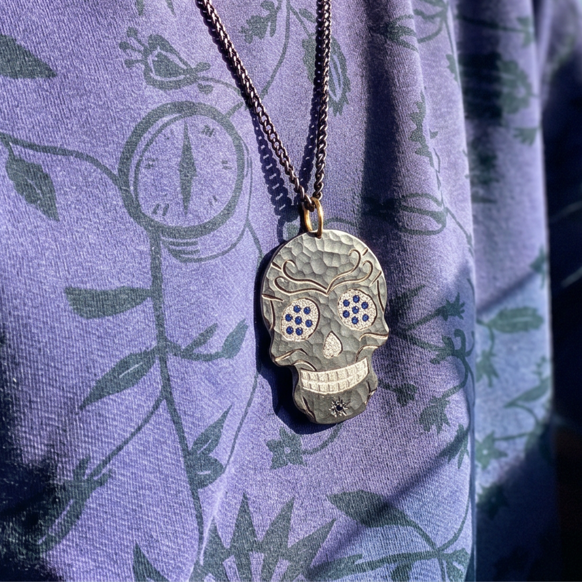 Skull-shaped pendant necklace on a purple fabric background with floral patterns