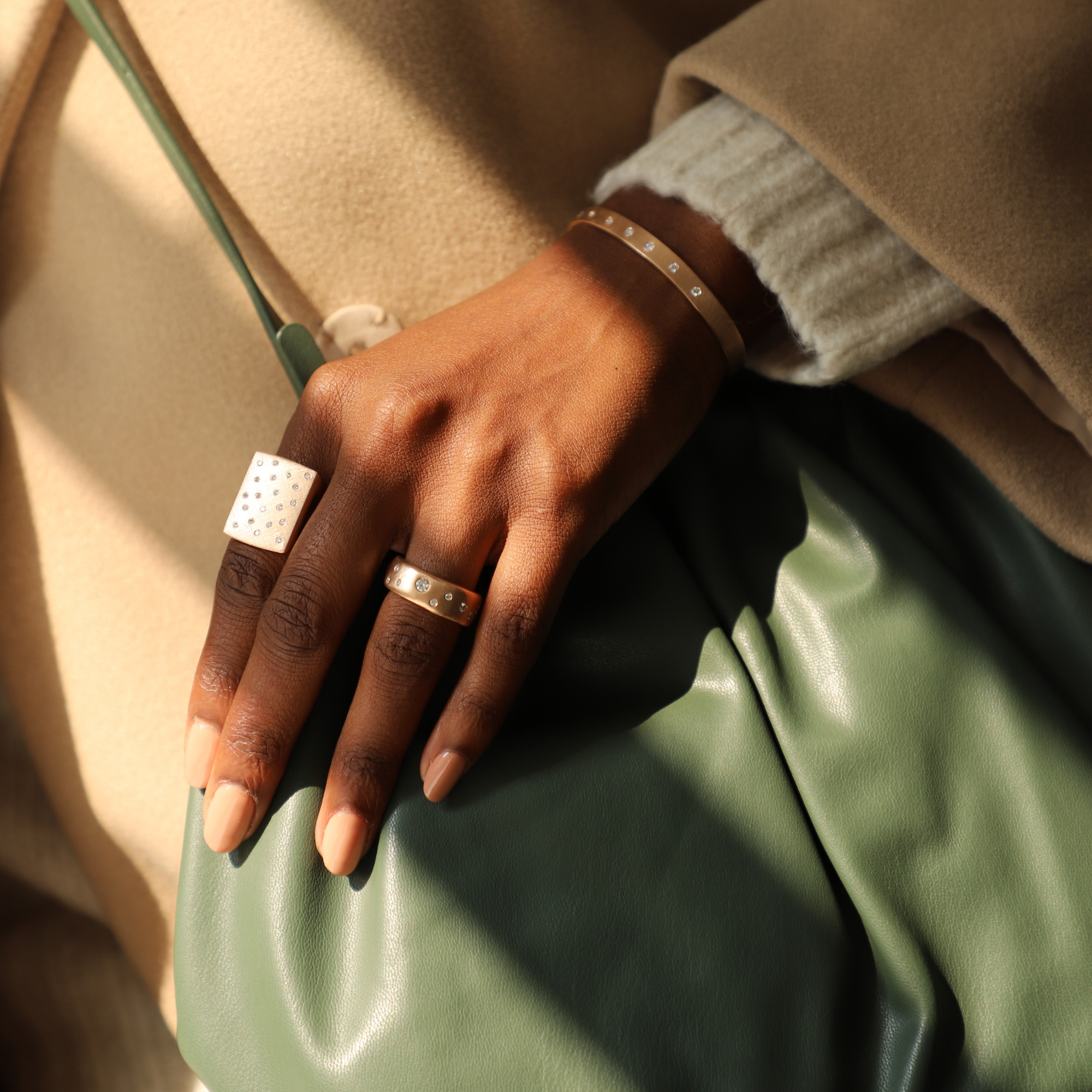 Model wearing chunky rose gold rings with scattered diamonds extra large block ring and complimenting wide band holding green purse