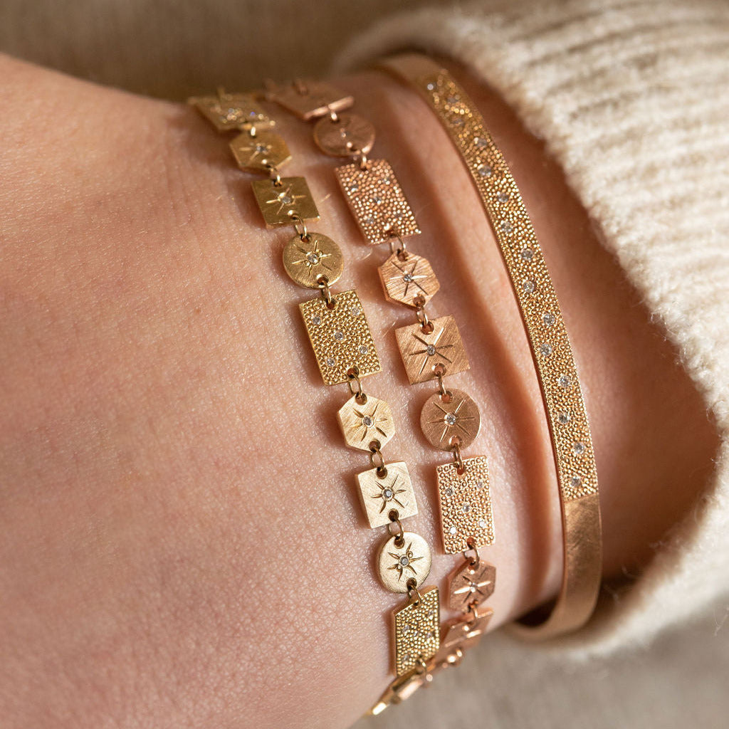 Close-up of a wrist wearing three gold bracelets with intricate designs.