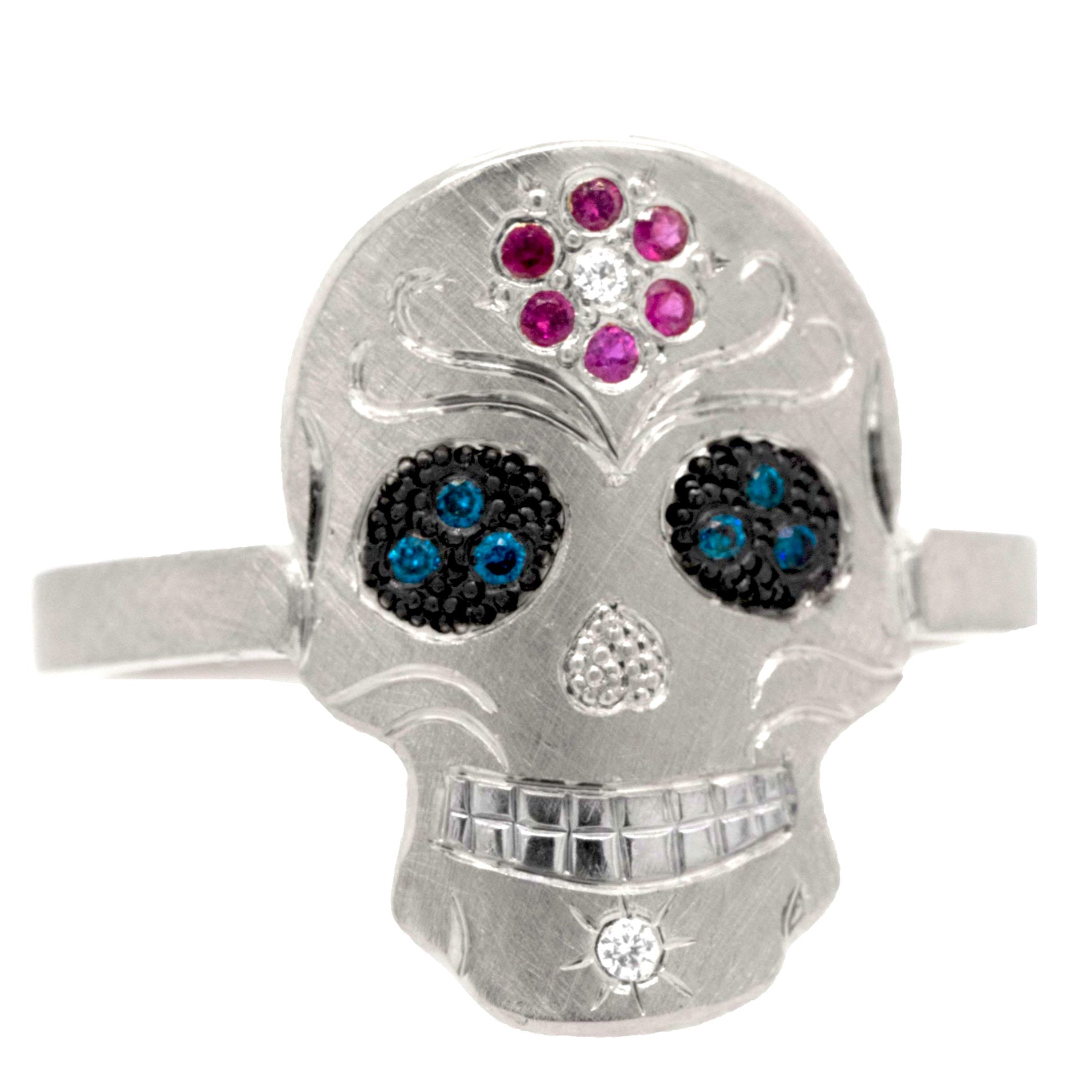 White gold skull-shaped ring with gemstones on a white background. Pave set pink sapphire flower on forhead, pave set eyes and diamond on chin. Fine engraving and milgrain detail.