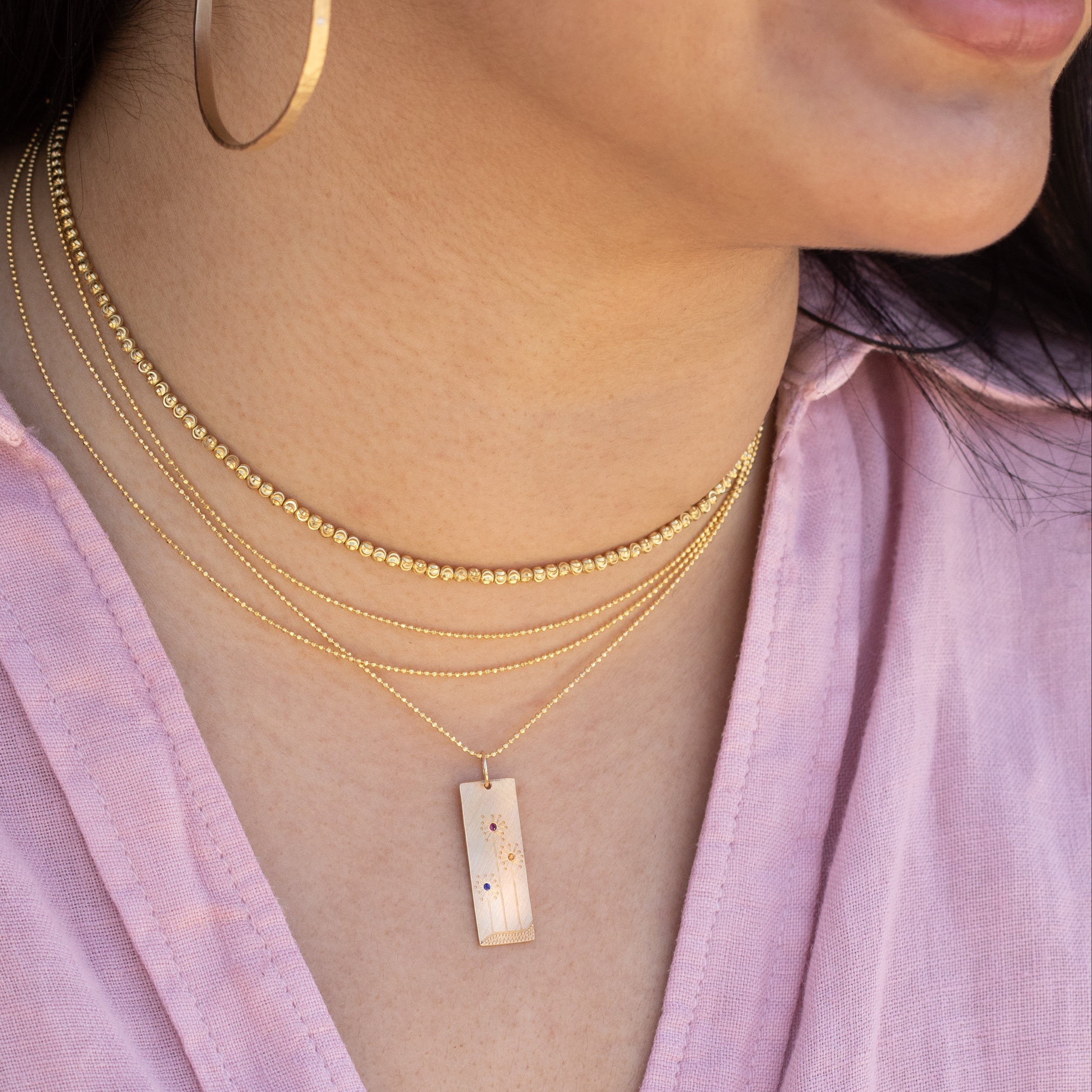 Lifestyle shot close up of model wearing layered 14k yellow gold diamond cut ball chain choker, mooncut faceted choker and floral bar pendant necklaces by Julez Bryant