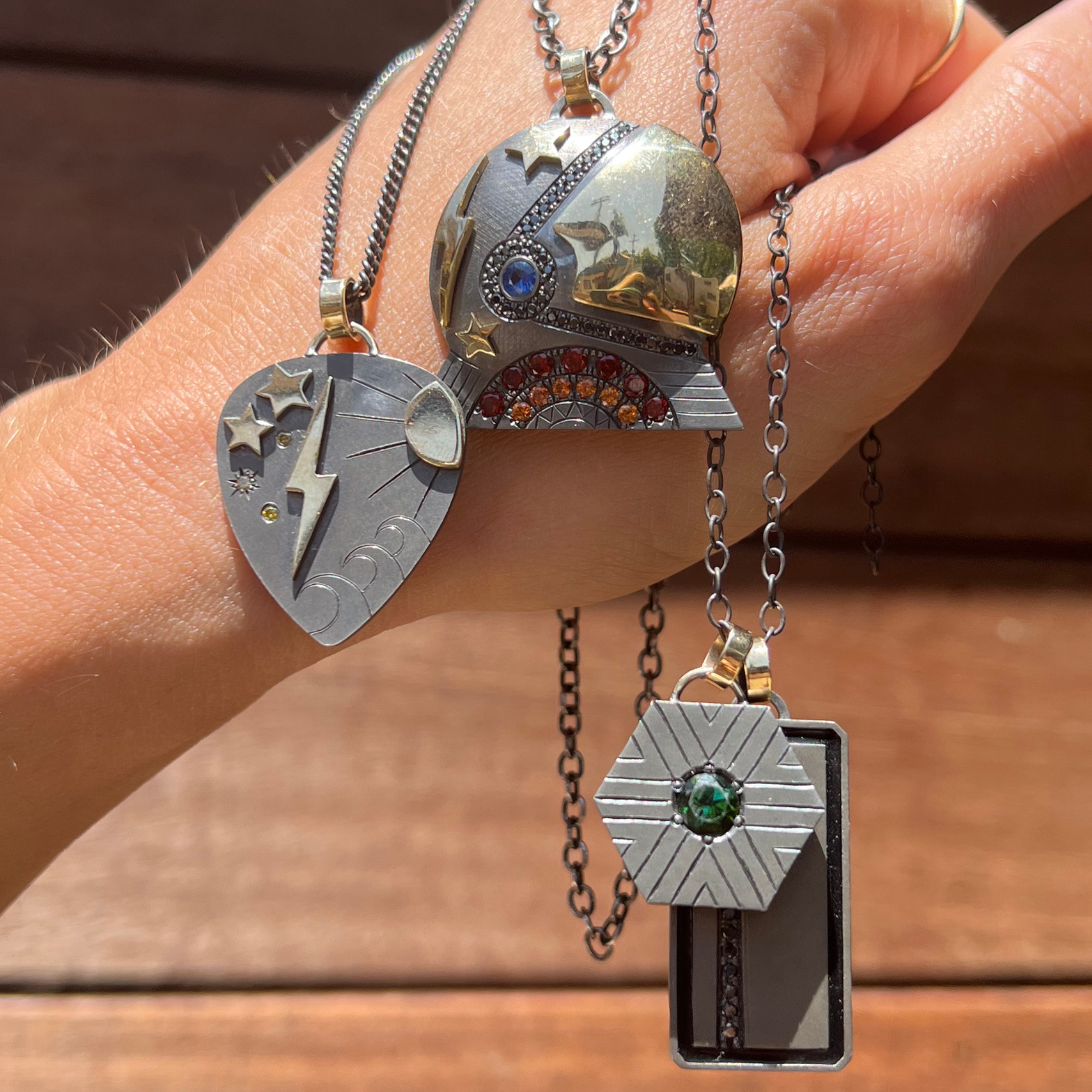 Image of a cosmic sterling silver 14k gold accent chunky geometric green and black diamond accent pendants held in hand with wood background.