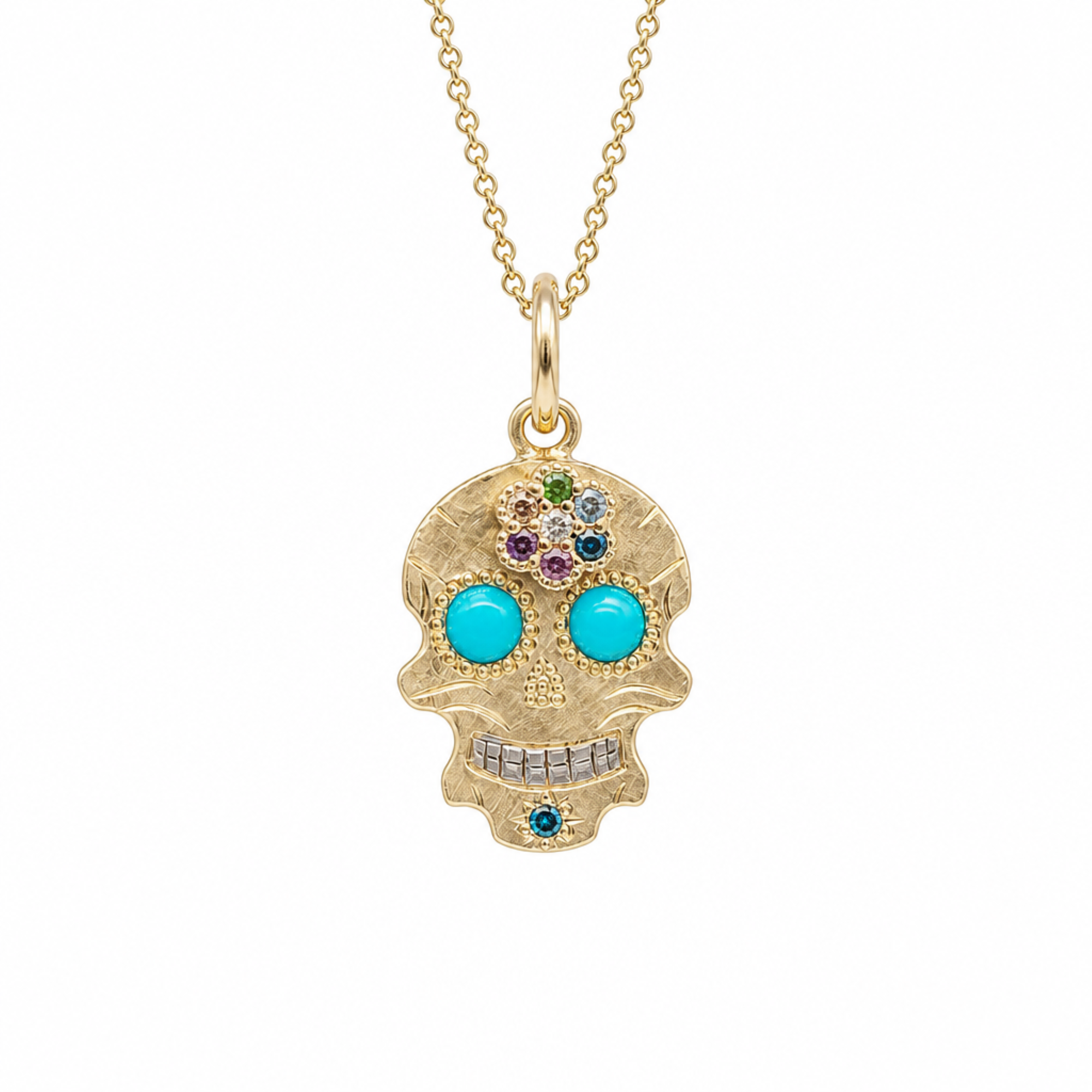 A gold sugar skull pendant necklace on a delicate gold chain, featuring turquoise-colored eyes and small multicolor gemstone accents on a plain white background.