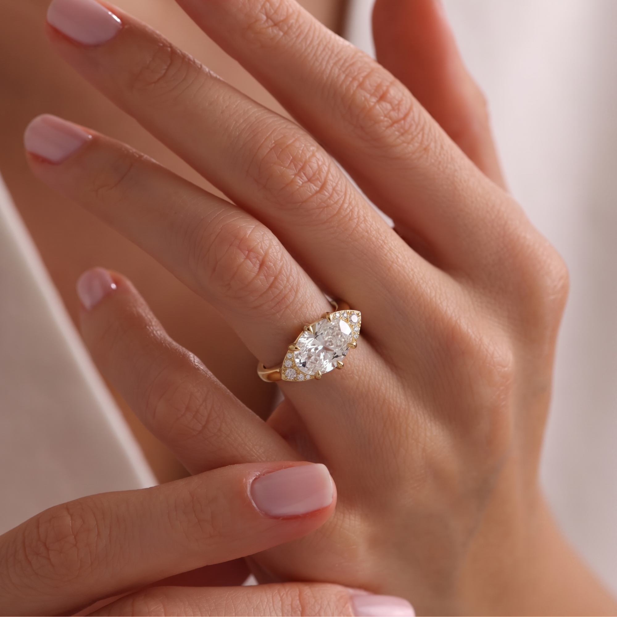 East-west oval white diamond cat eye half halo engagement ring in 14k yellow gold, lifestyle shot worn on a model's hand