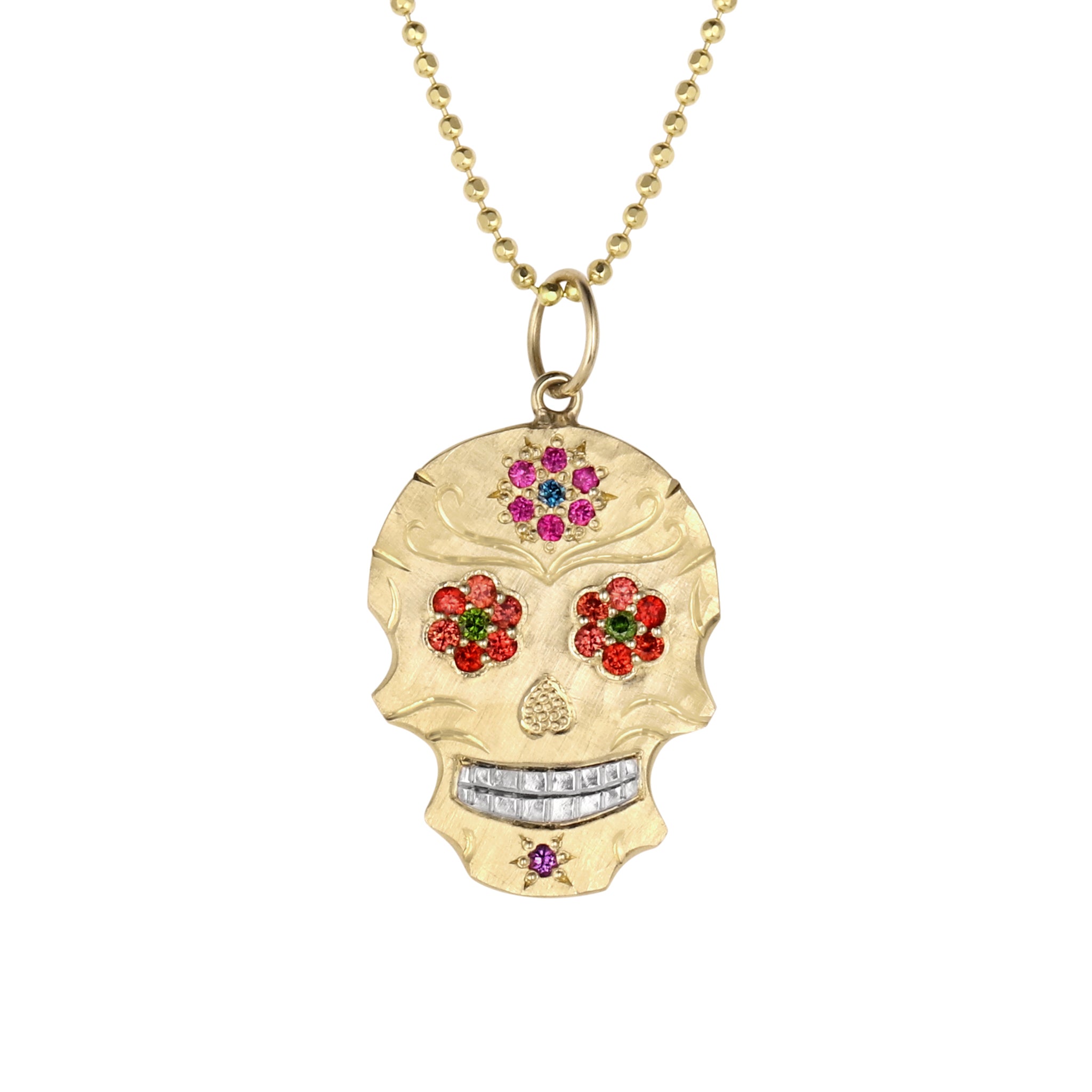 Small 14k gold skull shaped pendant necklace with red and green bezel set gemstone floral eyes, bead set pink and blue flower on forehead, purple stone on chin, hand engraved details and shiny rhodium plated teeth hanging on 14k gold ball chain shown on a white background.
