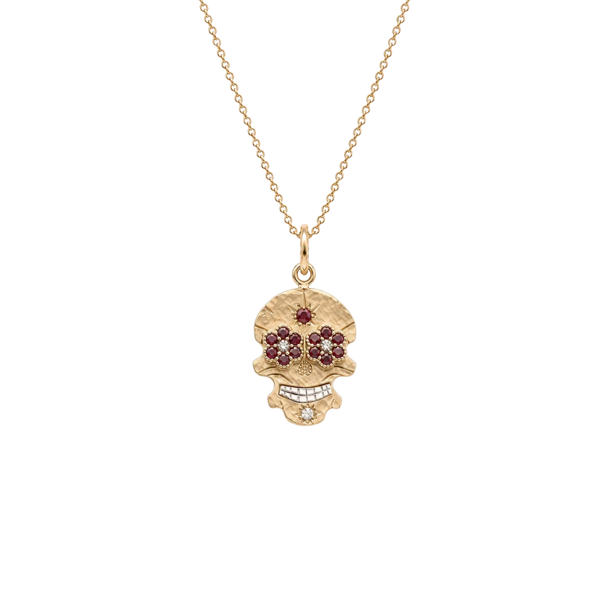 A gold skull pendant necklace featuring dark red gemstone eyes and a small clear stone on the teeth, suspended from a delicate gold chain against a plain white background.
