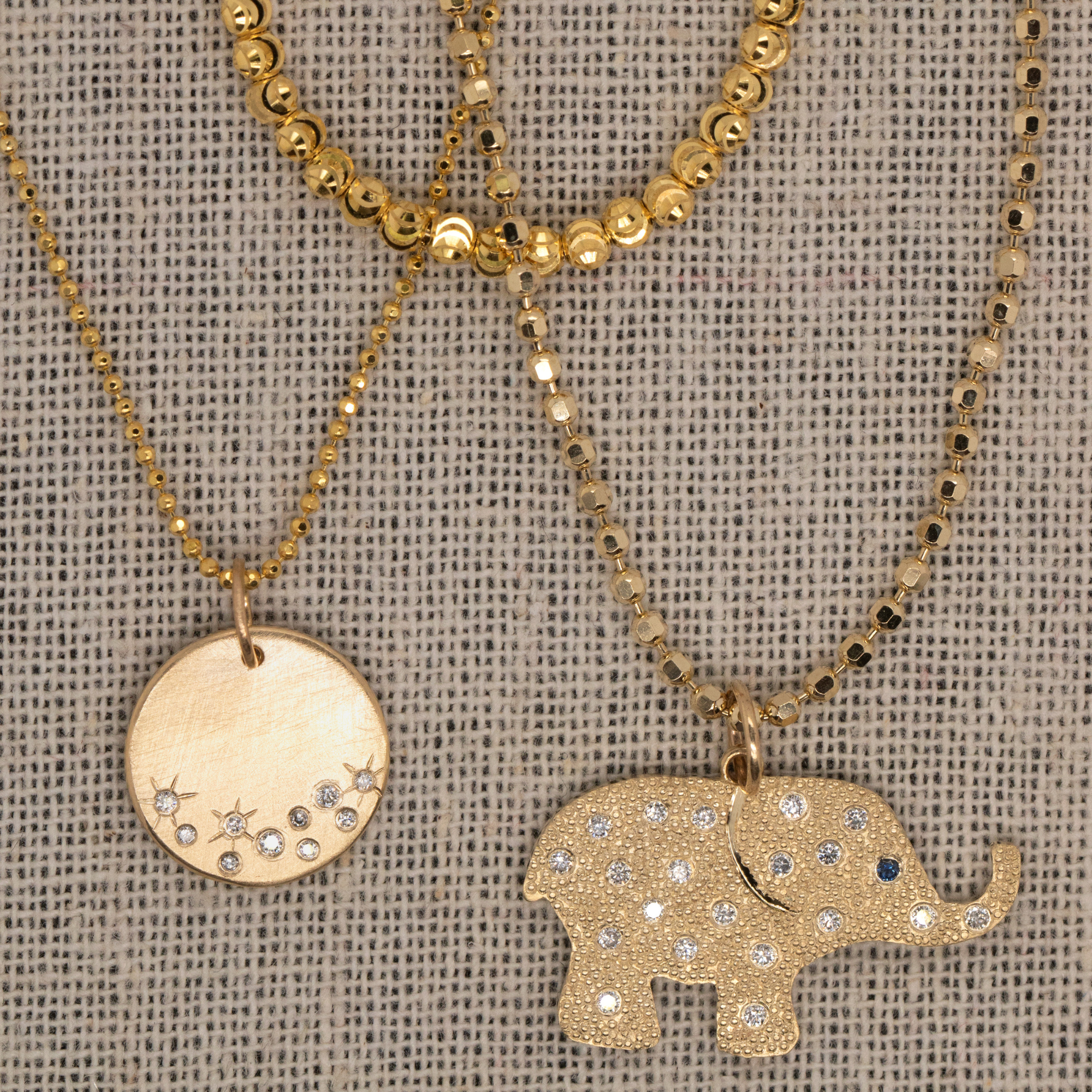 14k yellow gold necklace stack including moca choker with beaded elephant charm and round medallion with white diamonds and starburst etching on gauze background