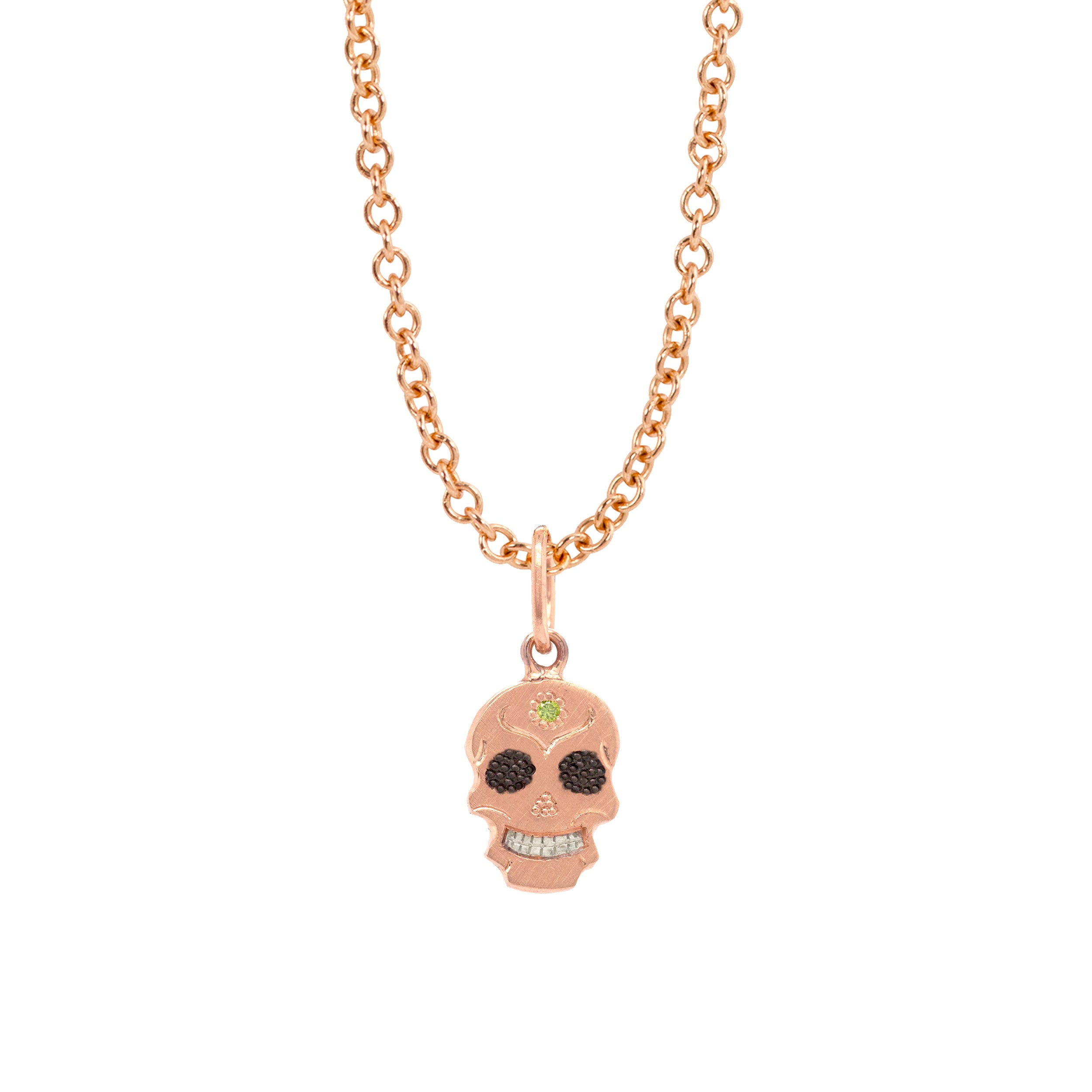 A Teeny Tiny collection rose gold charm in the shape of a sugar skull with a round apple green diamond in the center, displayed on a gold chain against a white background.