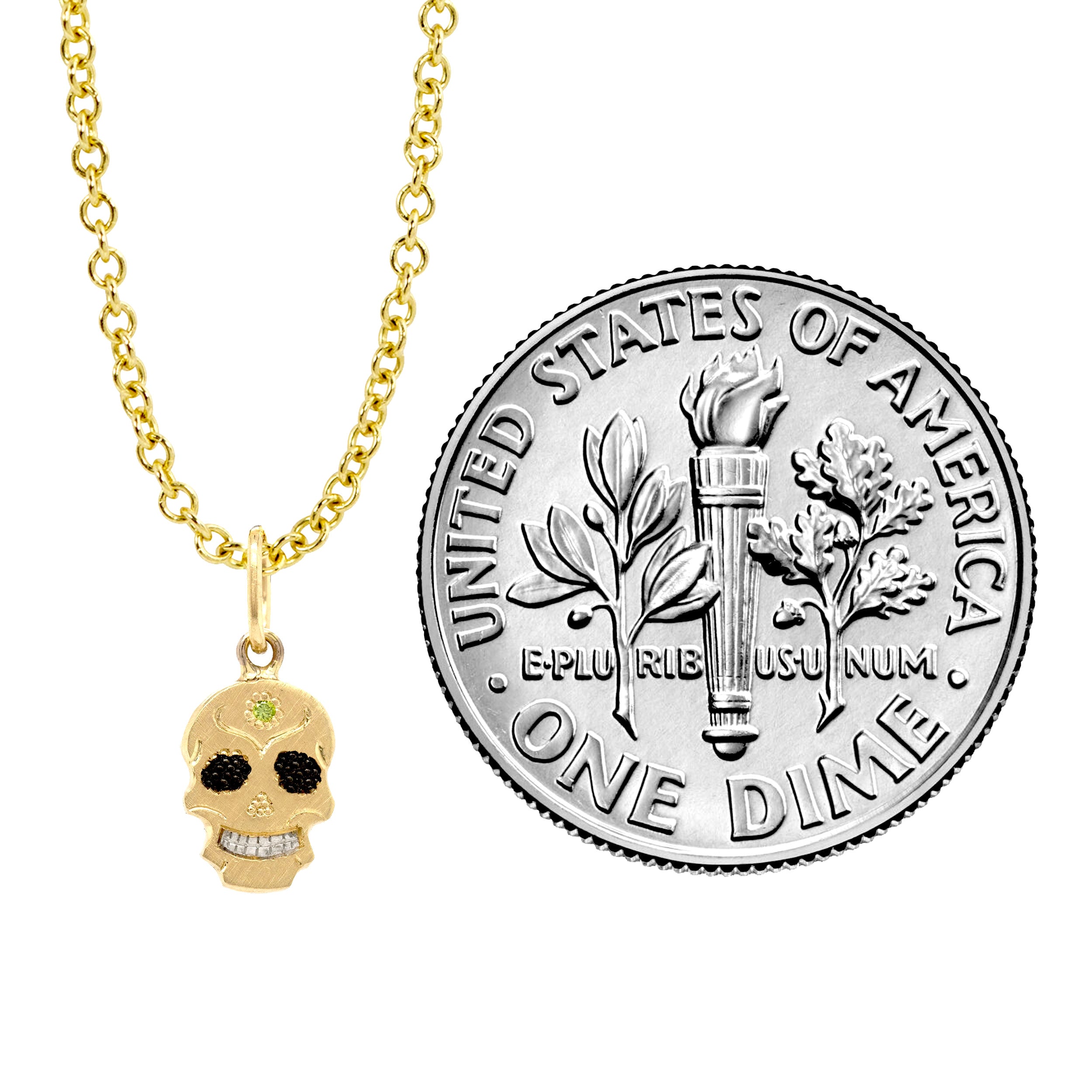 A Teeny Tiny collection gold charm in the shape of a sugar skull with a round apple green diamond in the center, displayed on a gold chain against a white background with dime for reference.