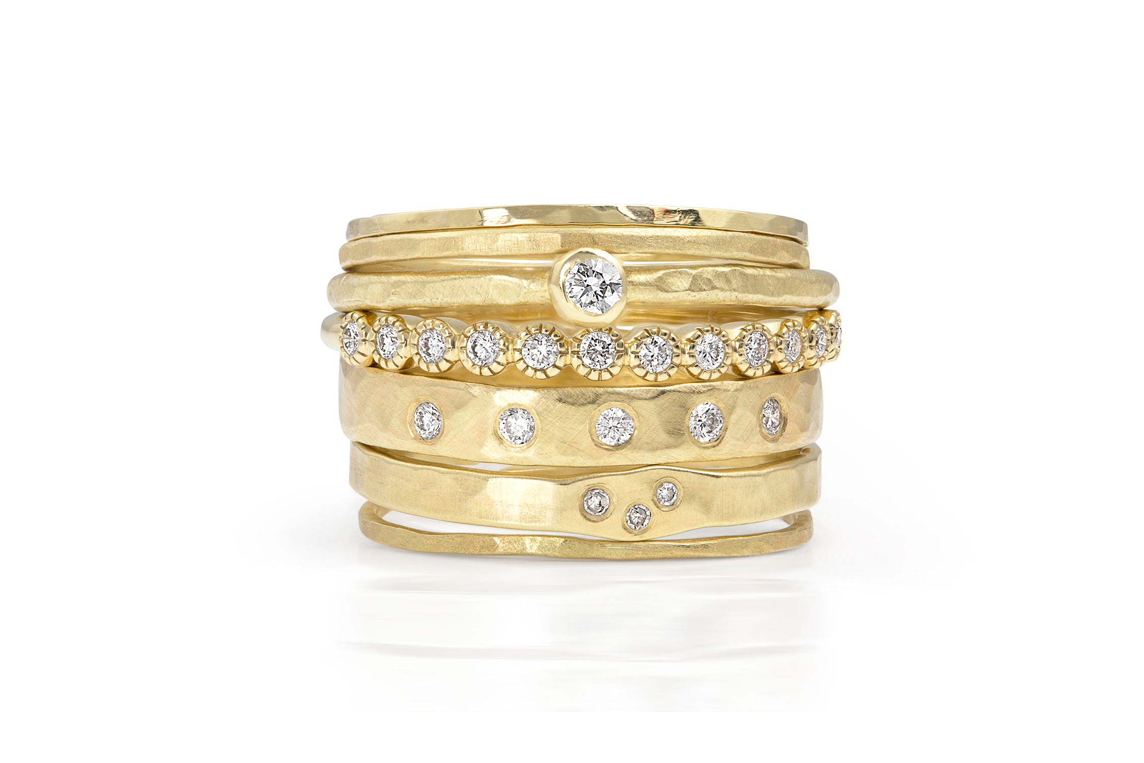 Stack of yellow gold rings ,bezel solitaire and scattered diamonds and hammered and milgrain texture on a white background