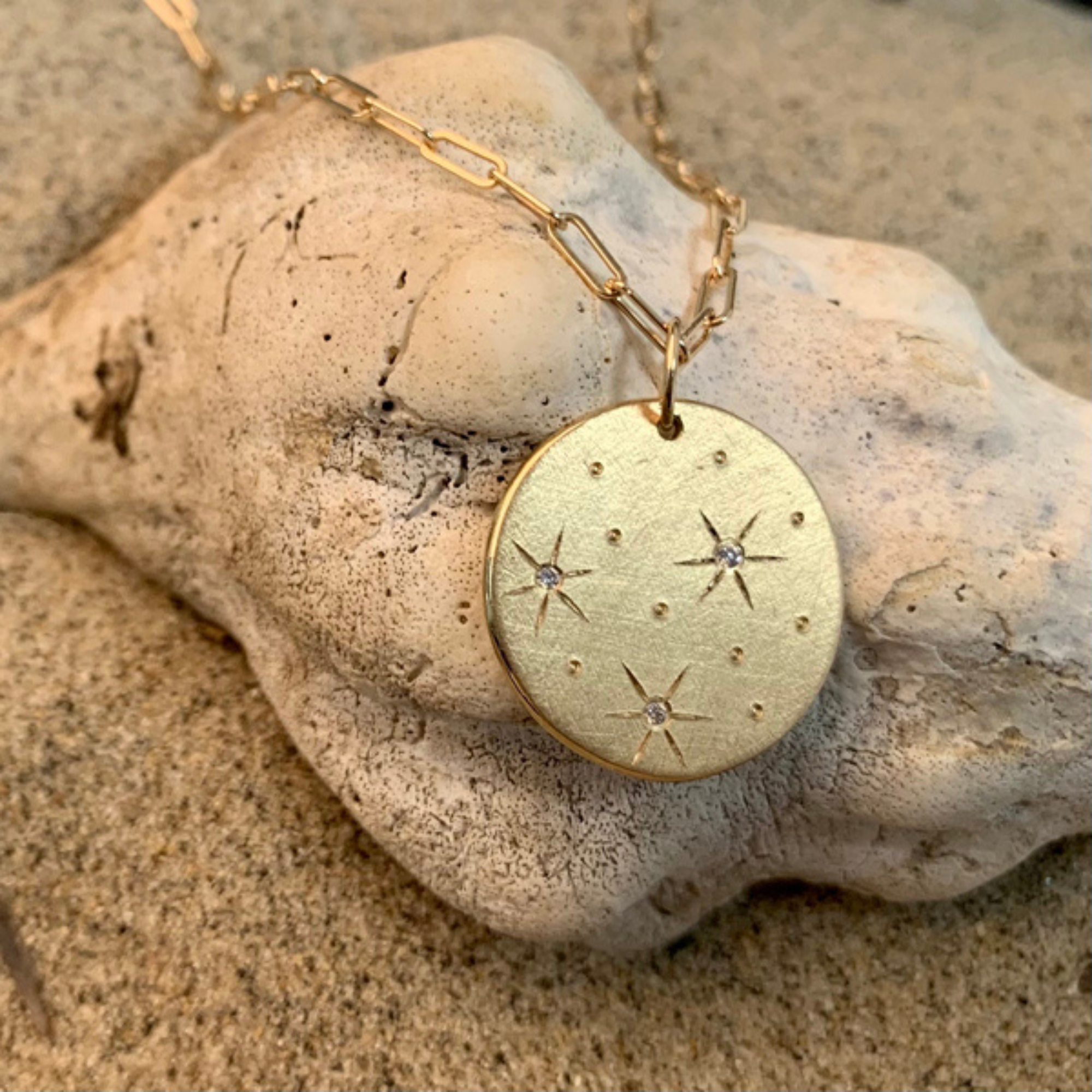 14k yellow gold satin round pendant featuring white diamond starburst designs on a link chain on a natural rock background