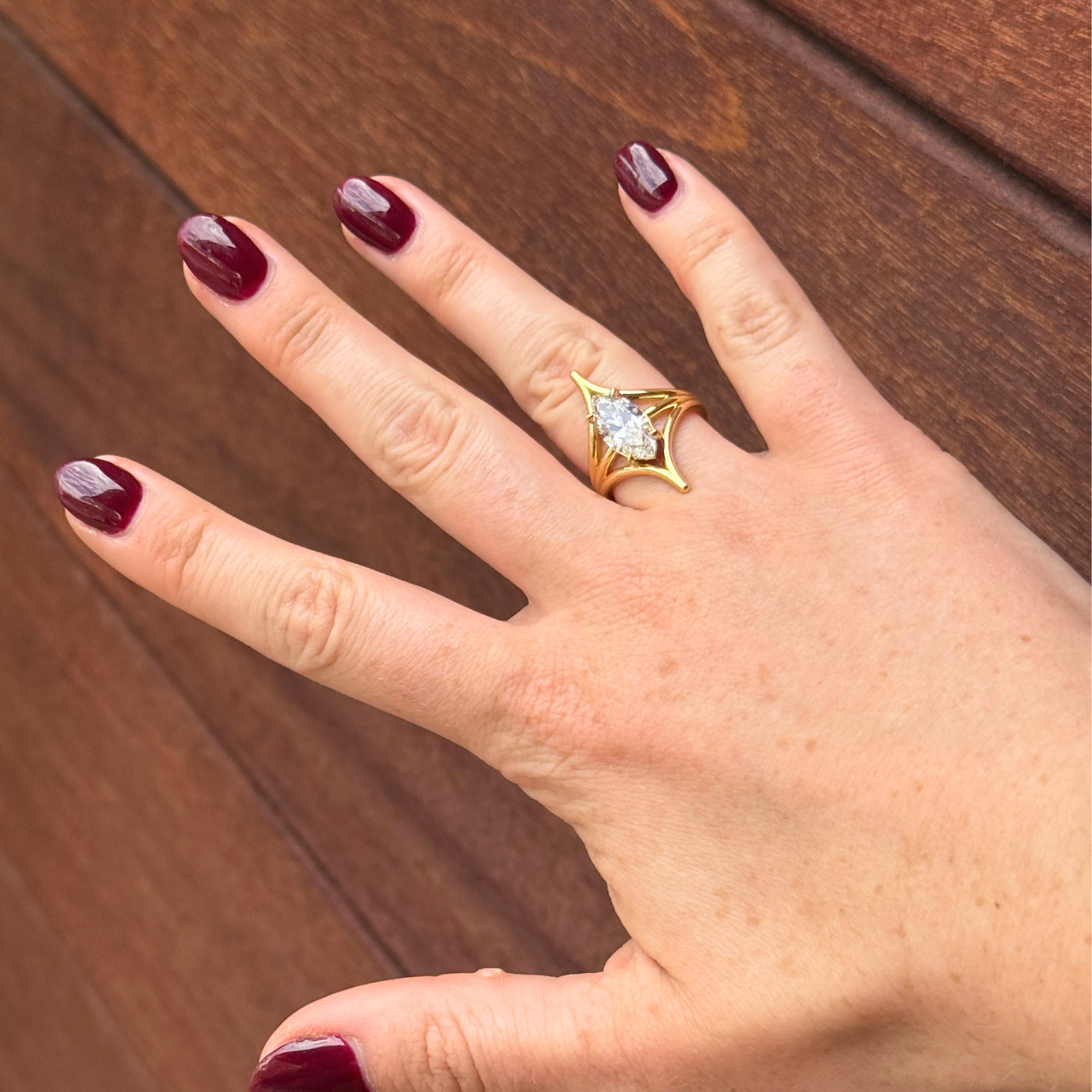 Lifestyle shot of a lab grown marquise open cage prong solitaire engagement ring 14k yellow gold candid wooden background.