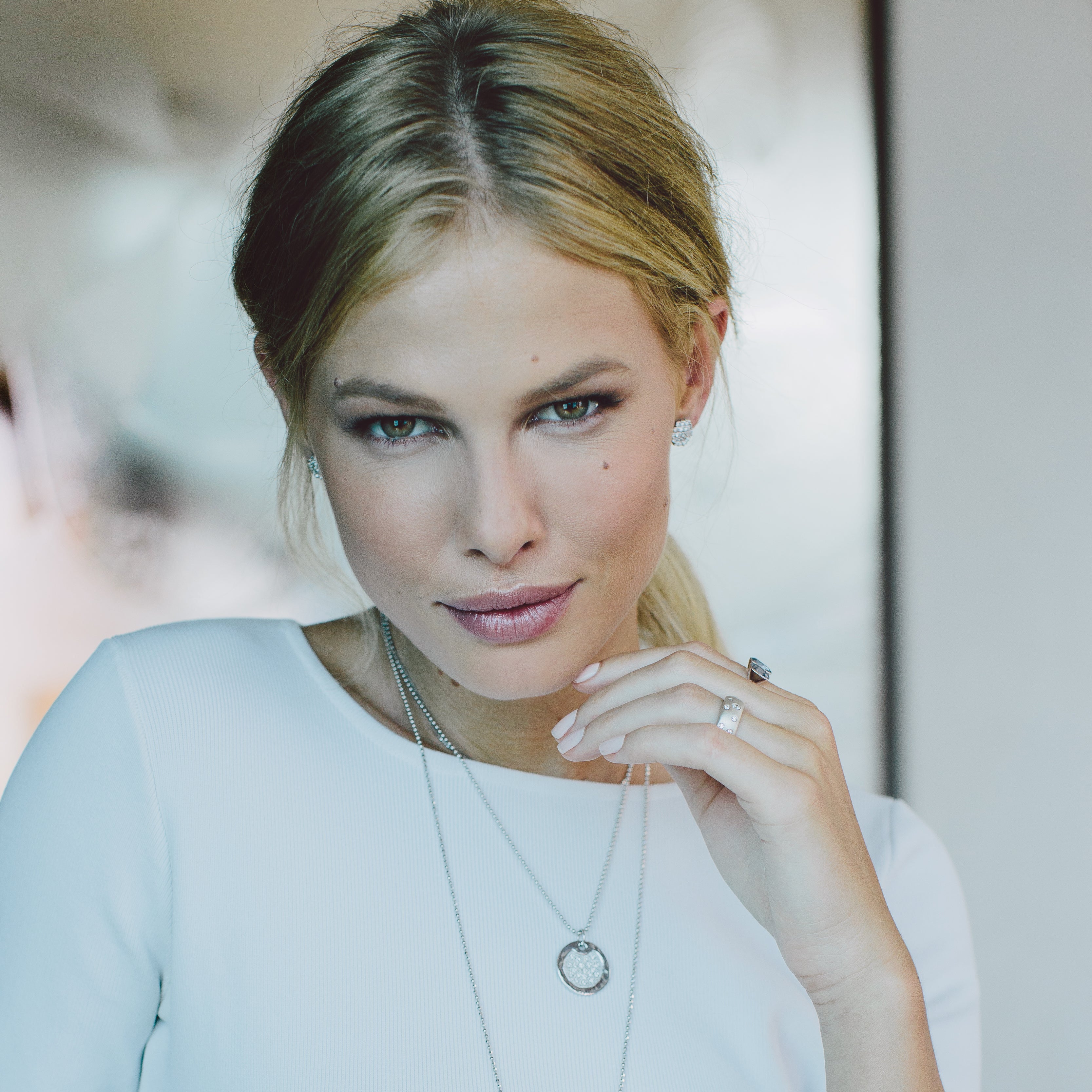Woman wearing white gold jewelry with diamonds, necklaces, rings, and earrings with a blurred background