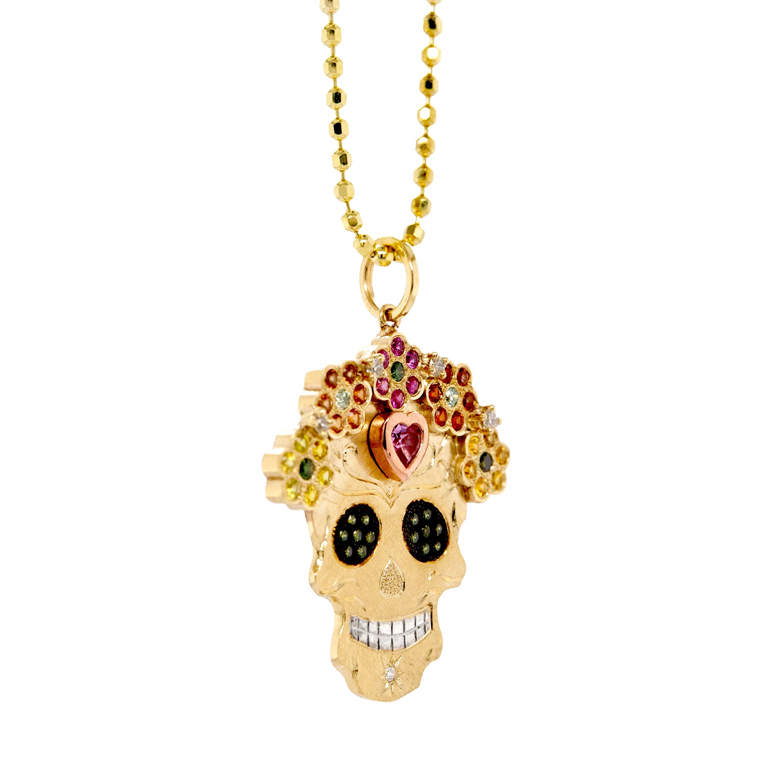 3/4 view of vibrant colorful Julez Bryant original Ghostrider Collection Mi Amore gemstone encrusted sugar skull extra large pendant. 14k solid yellow gold mixed diamond sapphires and Tzavorite. Fine detail engraving highlights features. Crown of flower clustered jewels in mixed colors. Rhodium blackened eyes with green Tzavorite pave set gemstone eyes. Large pink sapphire bezel set on forehead with rose gold border. Shown on 2.0mm ball chain.
