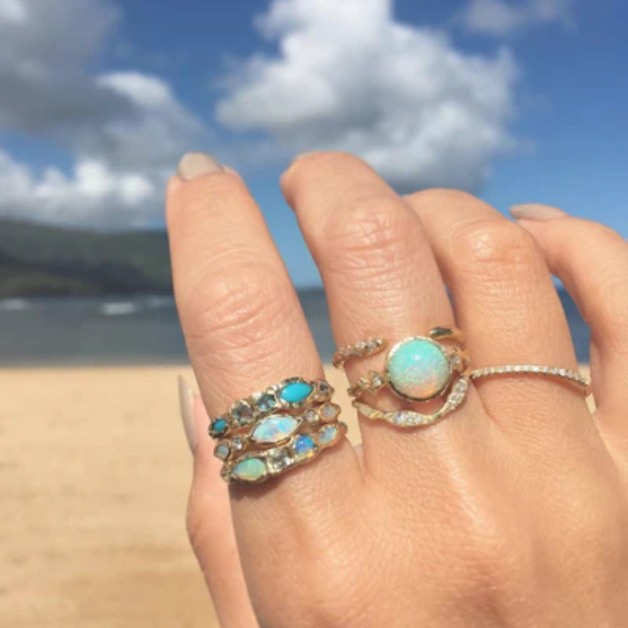 14k yellow gold lava ribbon ring by misa with white diamonds stacked with other misa rings on beach background on model in lifestyle shot