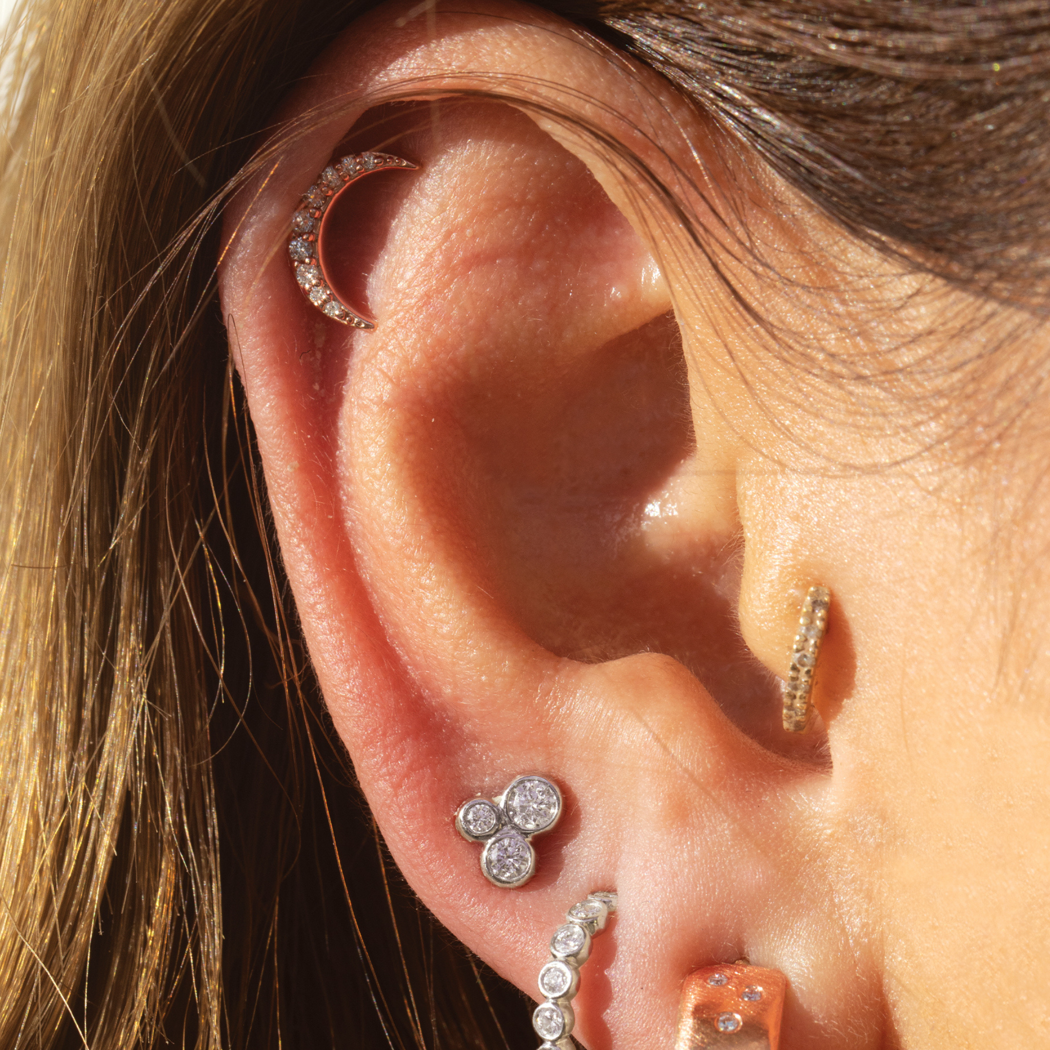 Close-up of an ear with multiple diamond earrings featuring.moon shaped pave diamond stud and three stone stud