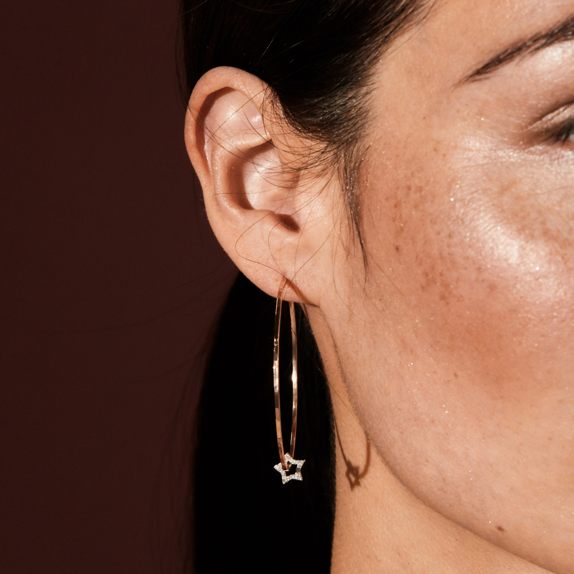 14k yellow gold hammered wire hoops with white gold pave white diamond star charms on model in lifestyle shot blurred background