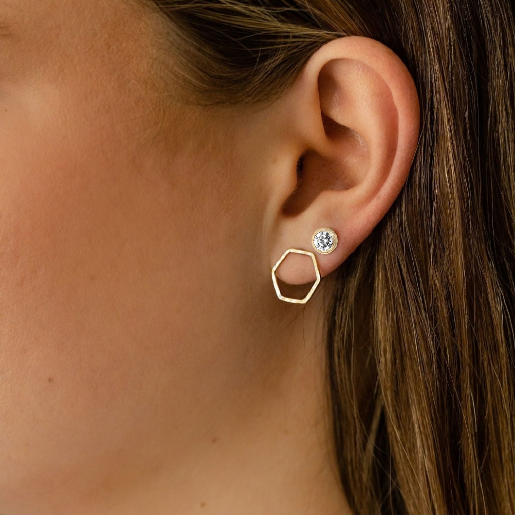 Close-up of a person wearing gold earrings with a bezel set diamond stud and an open hexagon post earring