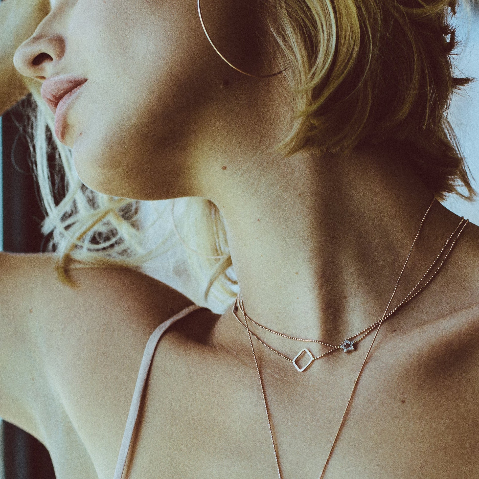 Close up of model with face to side showing layered choker necklaces in 14k rose gold one hammered texture open square and one pave diamond star charm integrated on diamond cut ball chain lifestyle shot