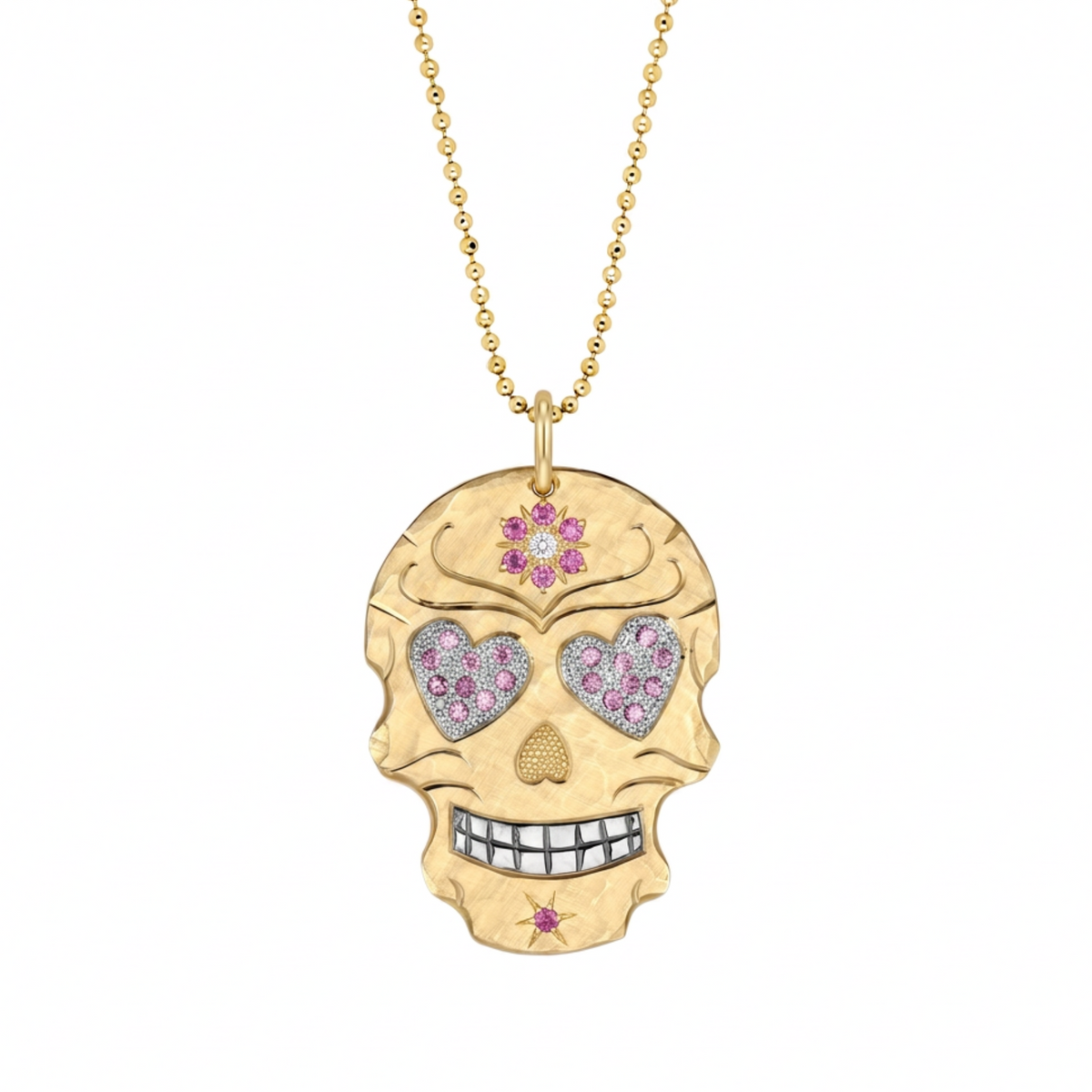 A gold skull pendant necklace on a gold ball chain, featuring heart-shaped eye sockets paved with pink and clear stones, and small pink gemstone accents on a white background.
