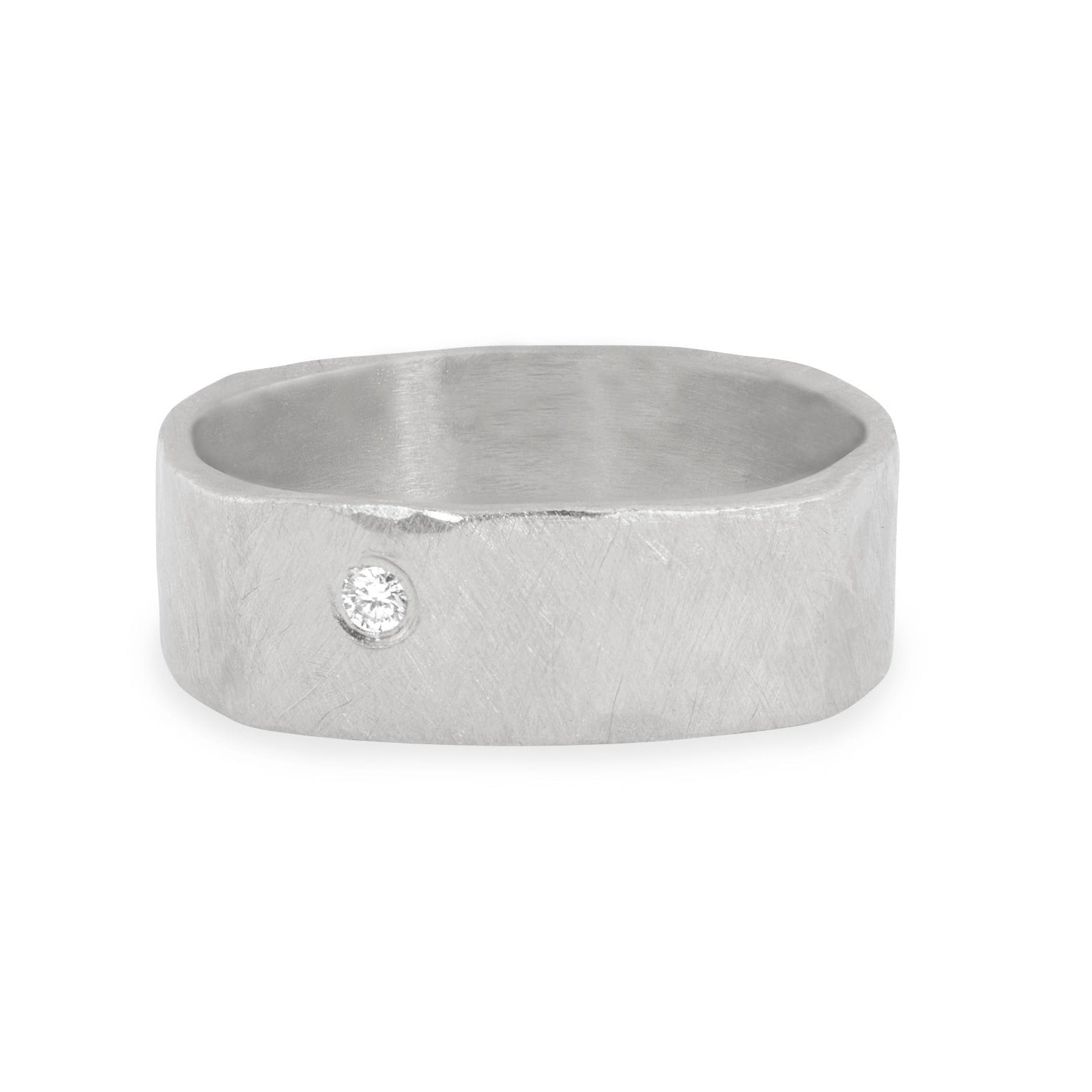 14k white gold heavyweight wide hammered brush textured band ring with offset white diamond single stone flush set in the face shown on white background